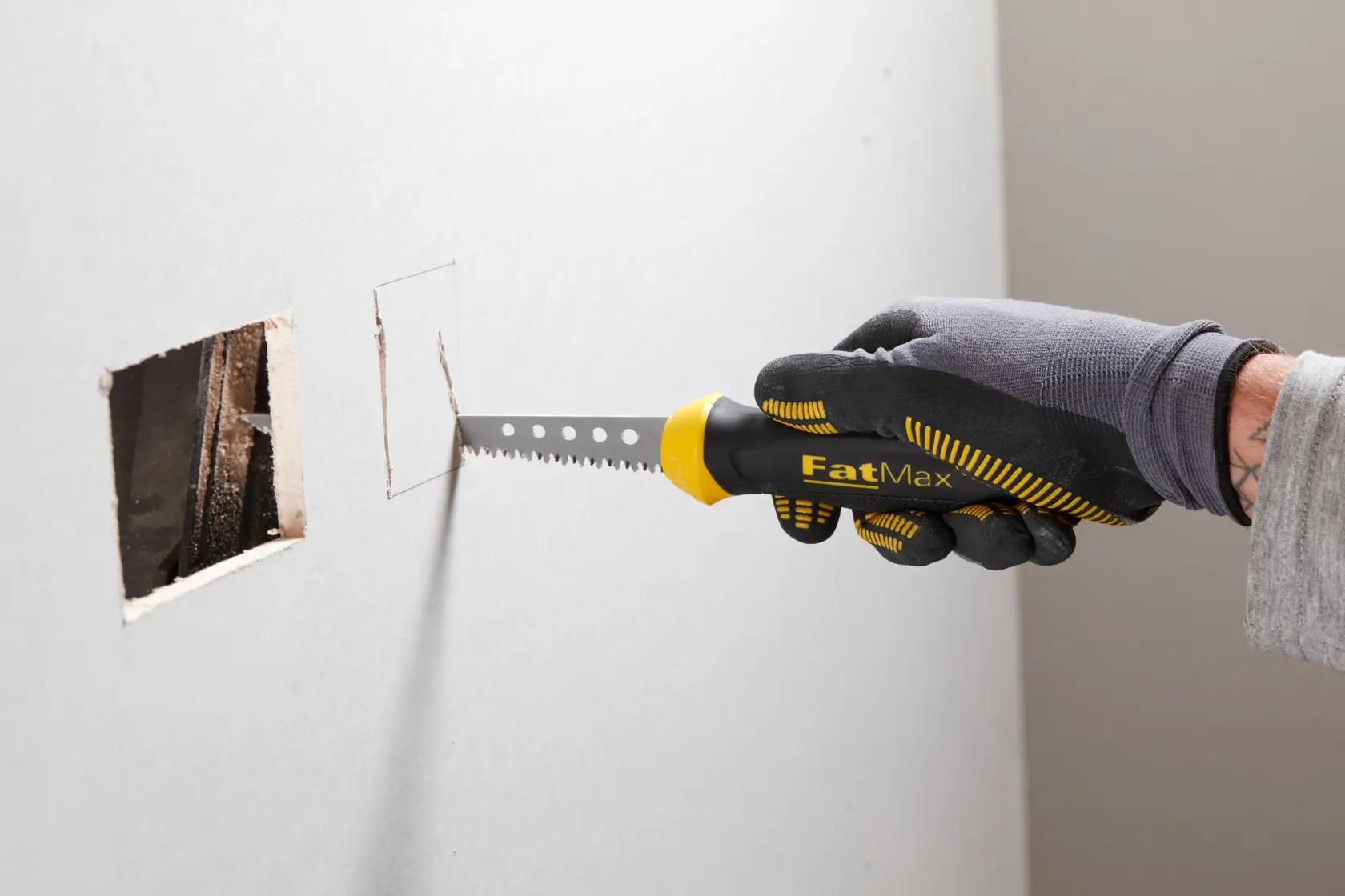 STANLEY 0-20-556 FatMax sierra para paneles de yeso cortando agujero rectangular en pared, vista lateral, mango negro y amarillo.