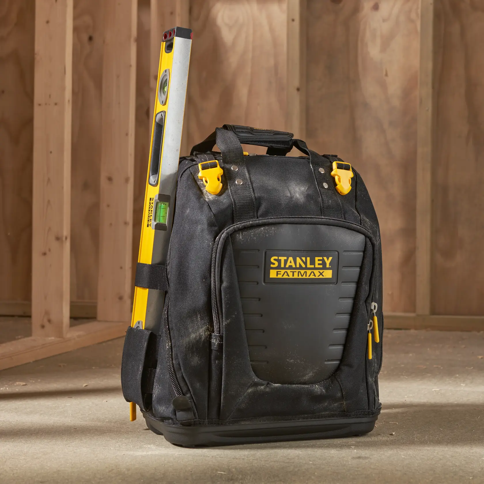 Mochila para herramientas STANLEY FMST1-80144 con nivel amarillo, mostrada en suelo de obra.