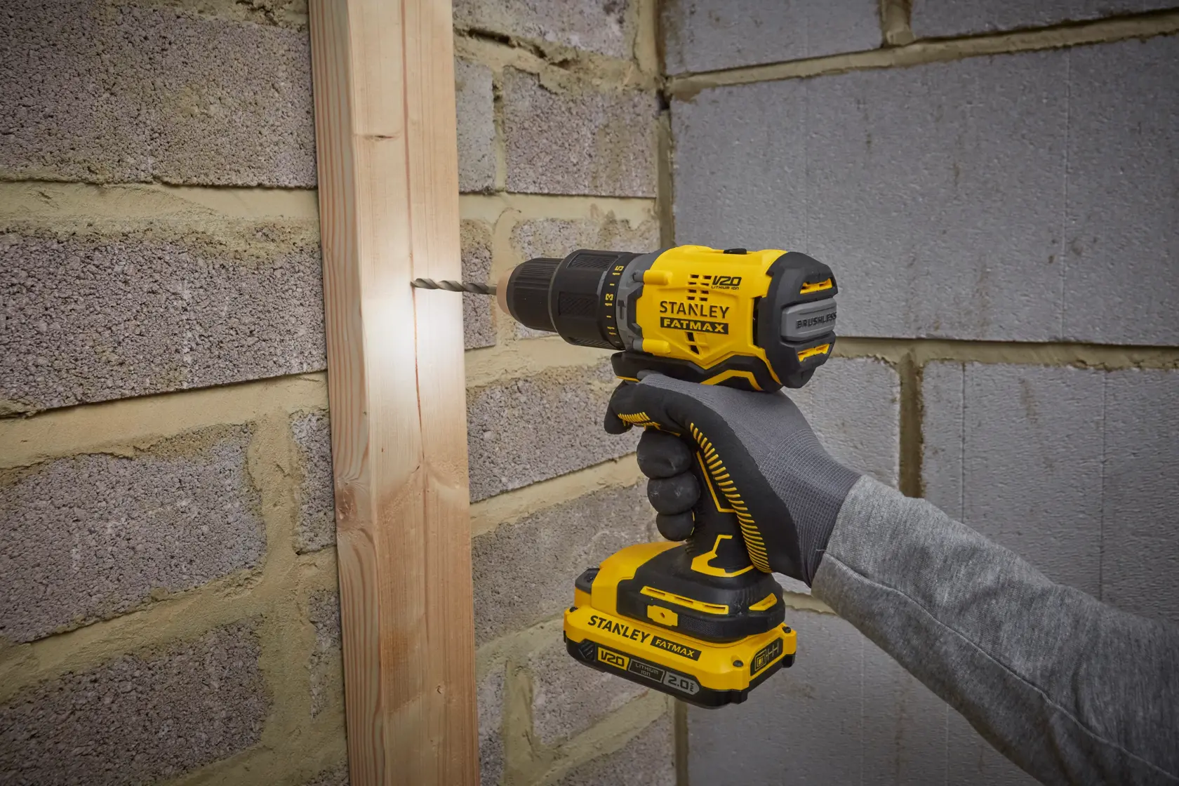 Taladro inalámbrico STANLEY SBD715C2K-B2 perforando madera sobre pared de ladrillo, vista lateral.