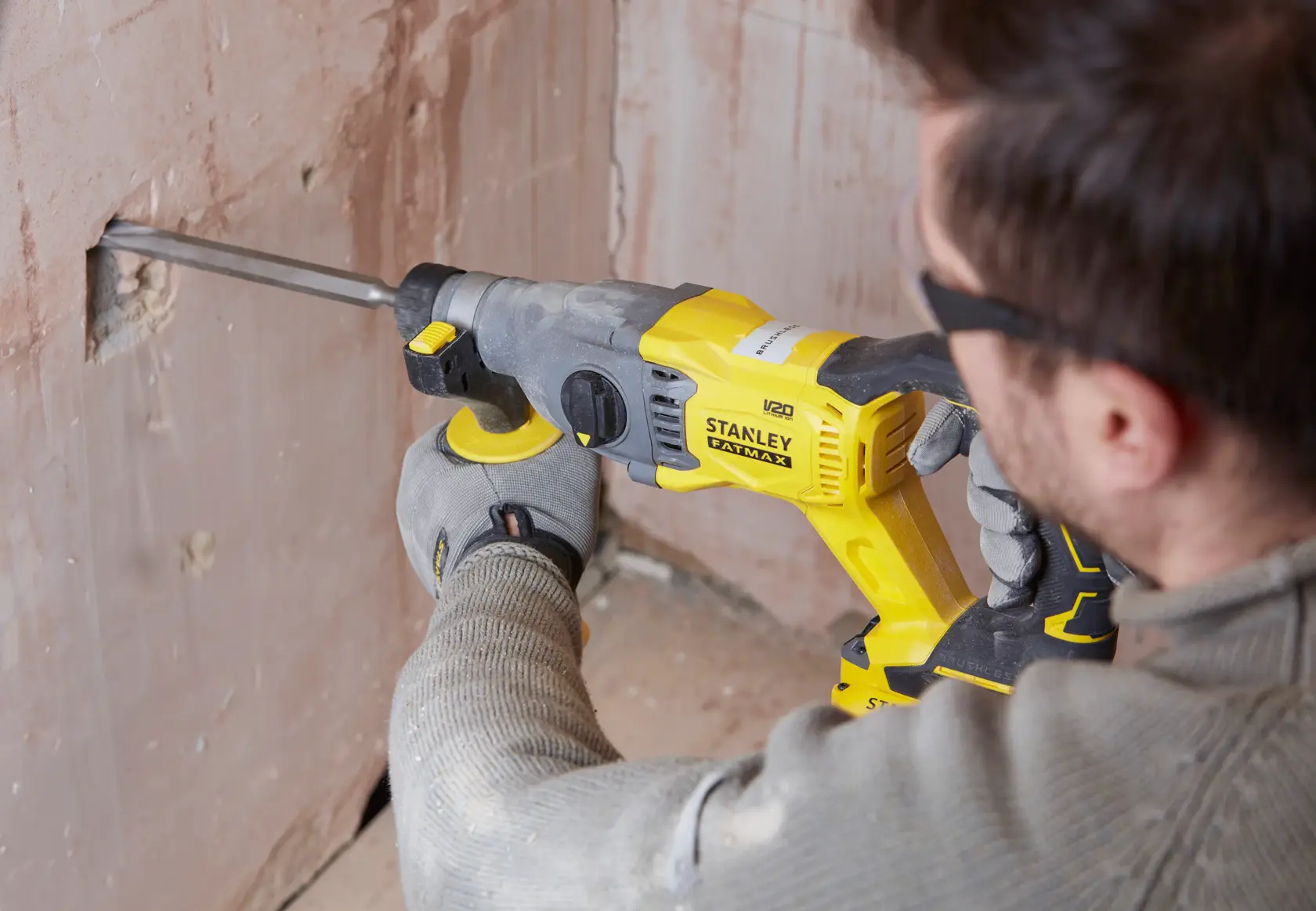 Martillo rotativo STANLEY SBH900M2K-B3 en uso perforando una pared, herramienta amarilla y negra sostenida por mano enguantada.