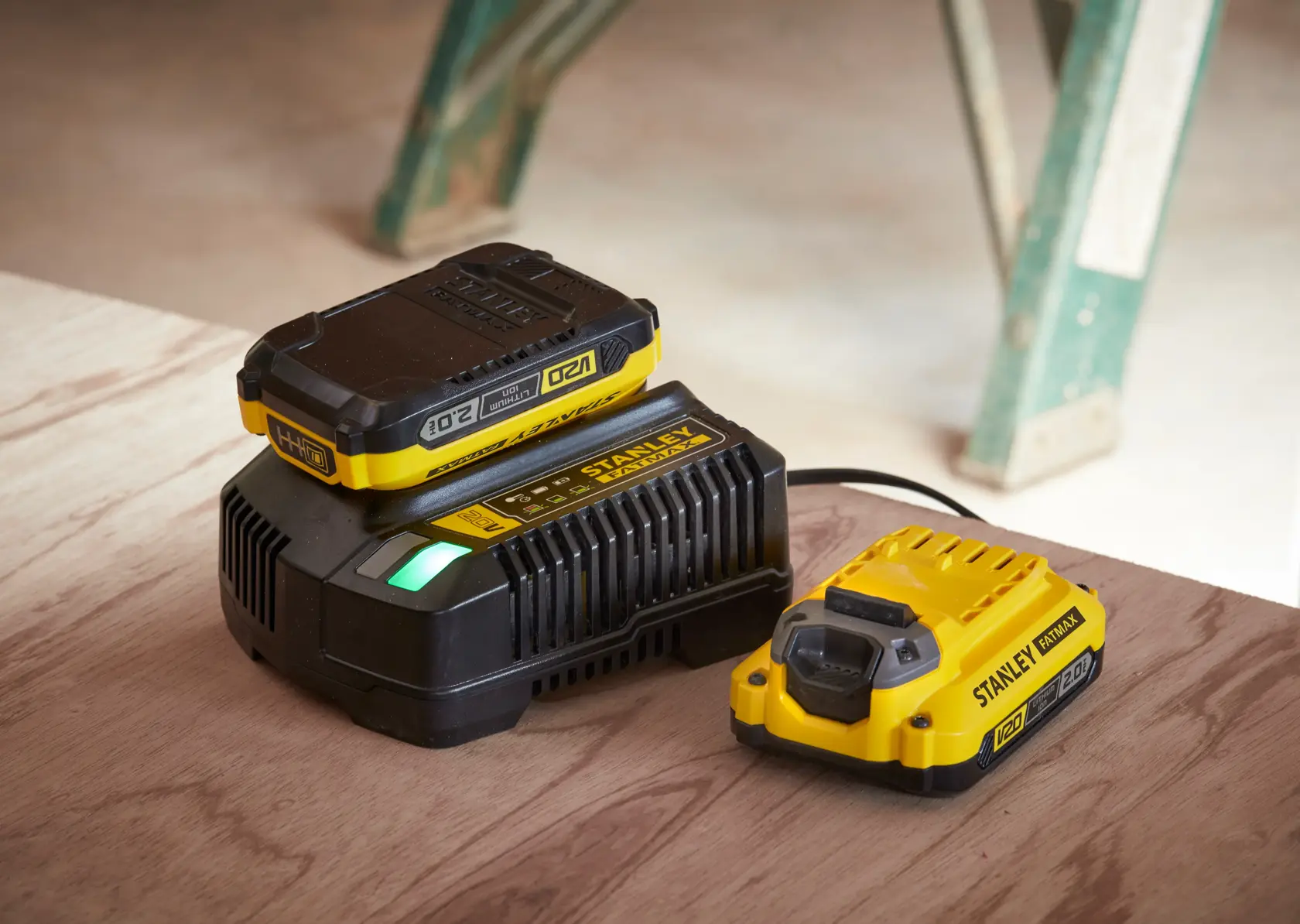 Cargador de batería y paquete de batería STANLEY SC200, amarillo y negro, vista en ángulo sobre superficie de madera.