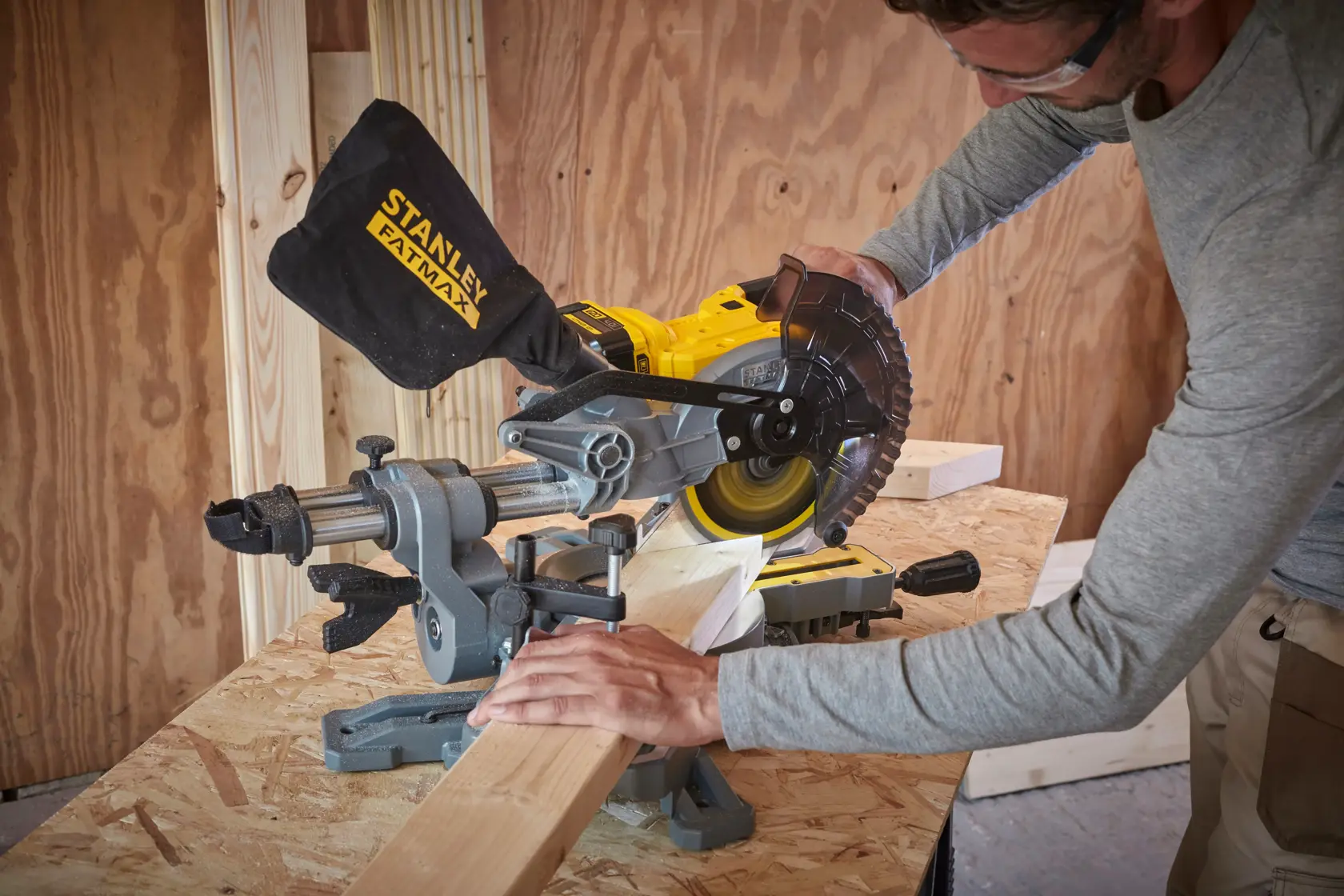 STANLEY SCM701-B3 sierra de inglete cortando madera en banco de trabajo, persona con gafas de seguridad.