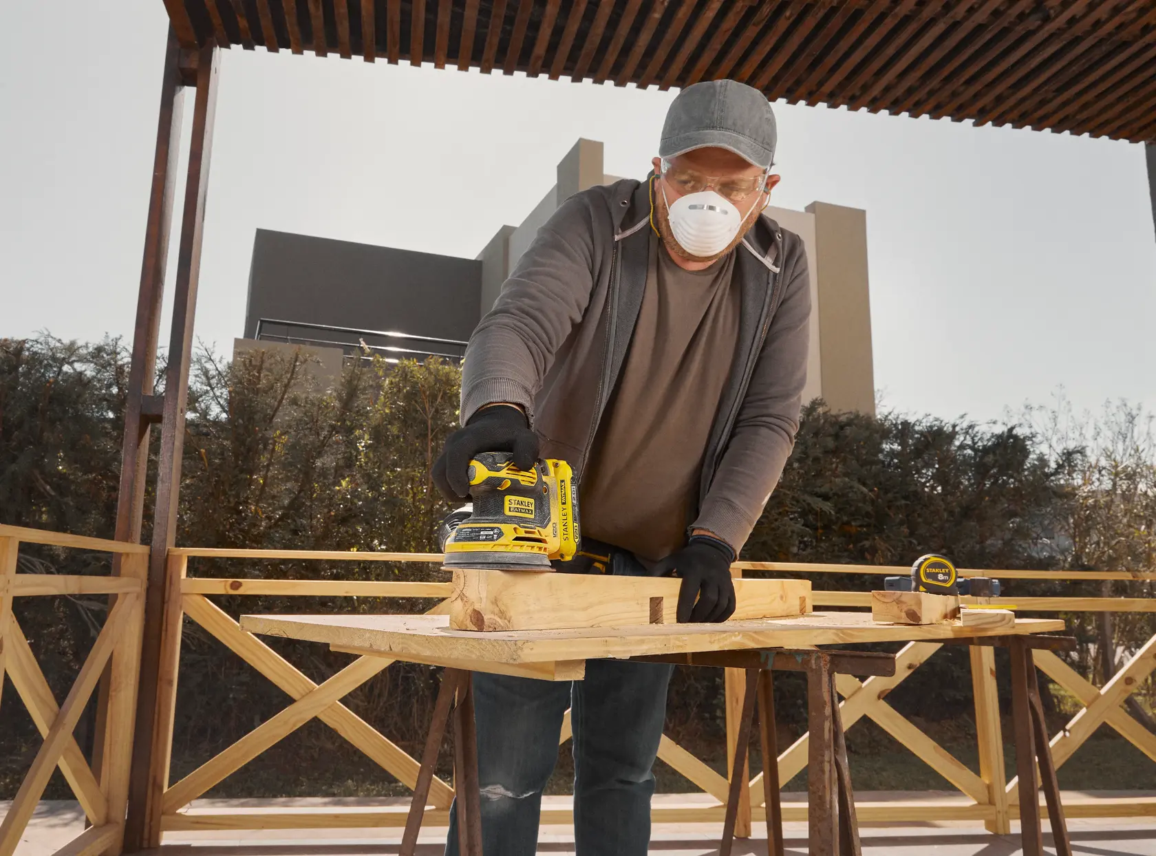 STANLEY SCS220B lijadora utilizada al aire libre sobre un banco de madera, con cinta métrica cercana.