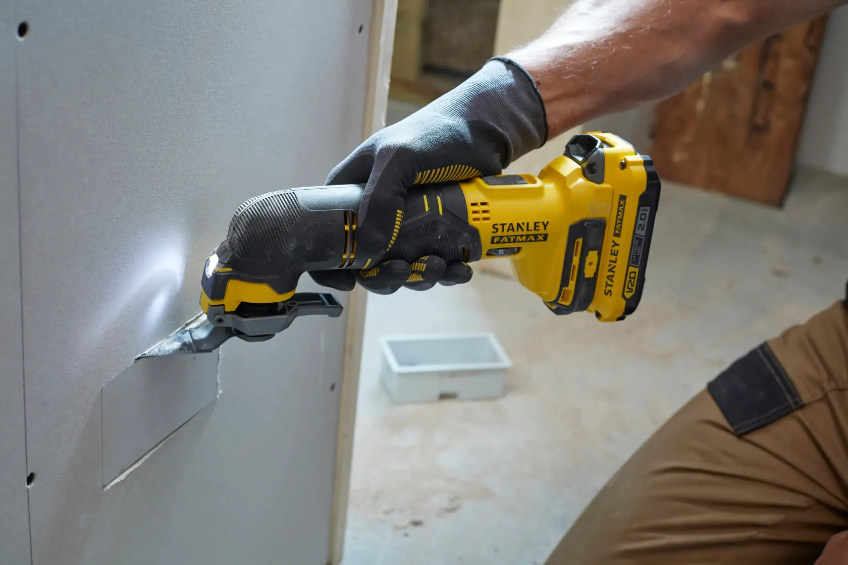 Herramienta oscilante Stanley SCT500D2K cortando panel de yeso, amarilla y negra, usada por trabajador con guantes.