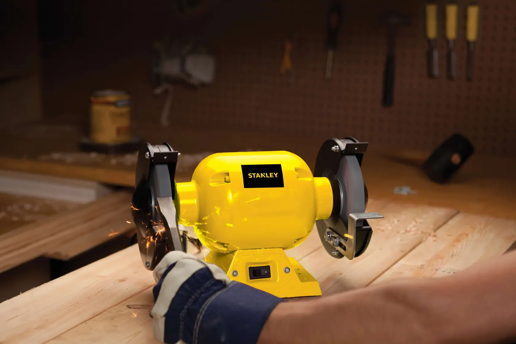 STANLEY STGB3715 esmeril de banco amarillo usado en un banco de trabajo de madera con chispas, ángulo lateral.