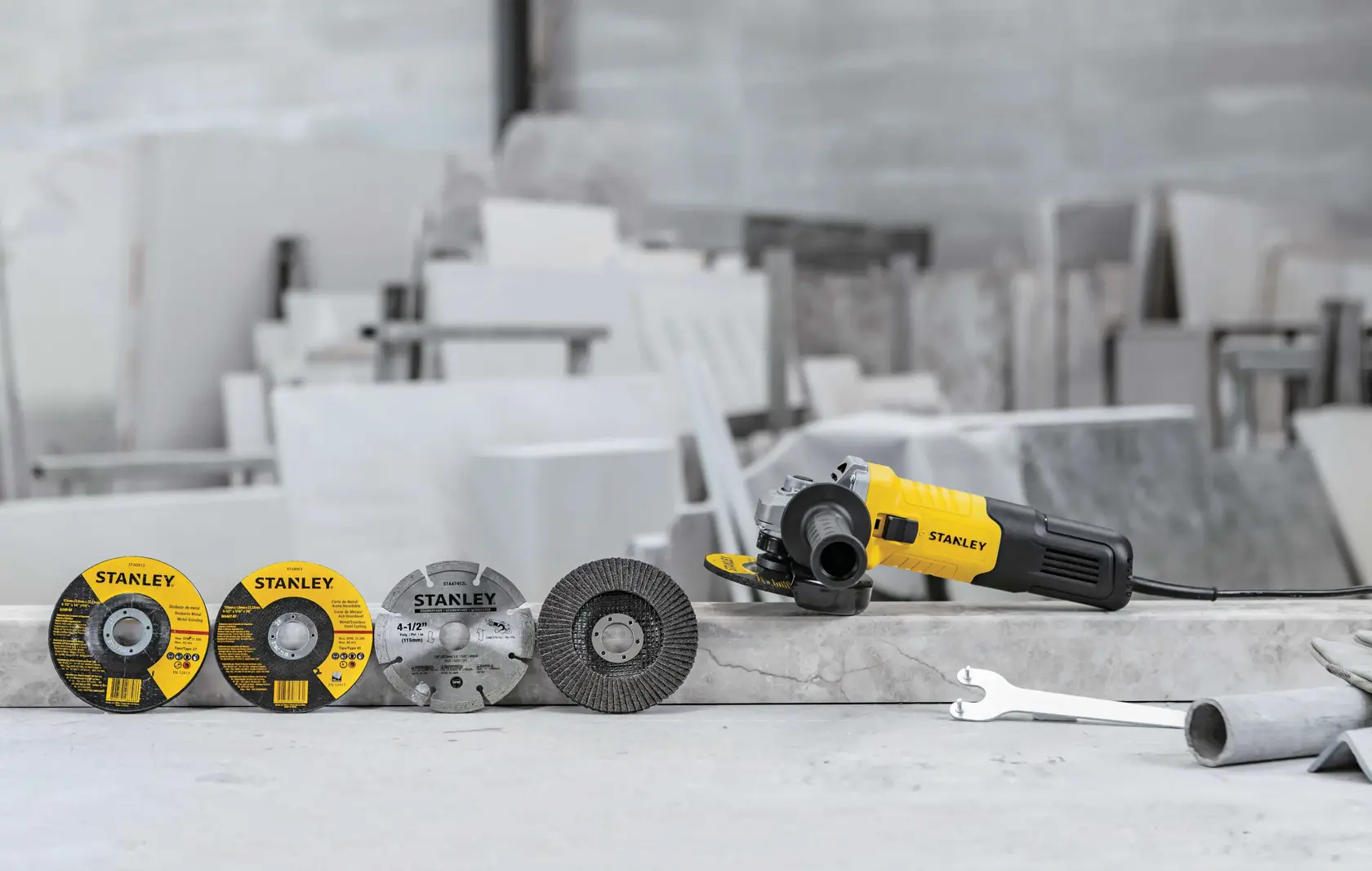 STANLEY STGS9100 esmeriladora angular con cuatro discos de corte y llave sobre superficie de piedra, vista lateral.