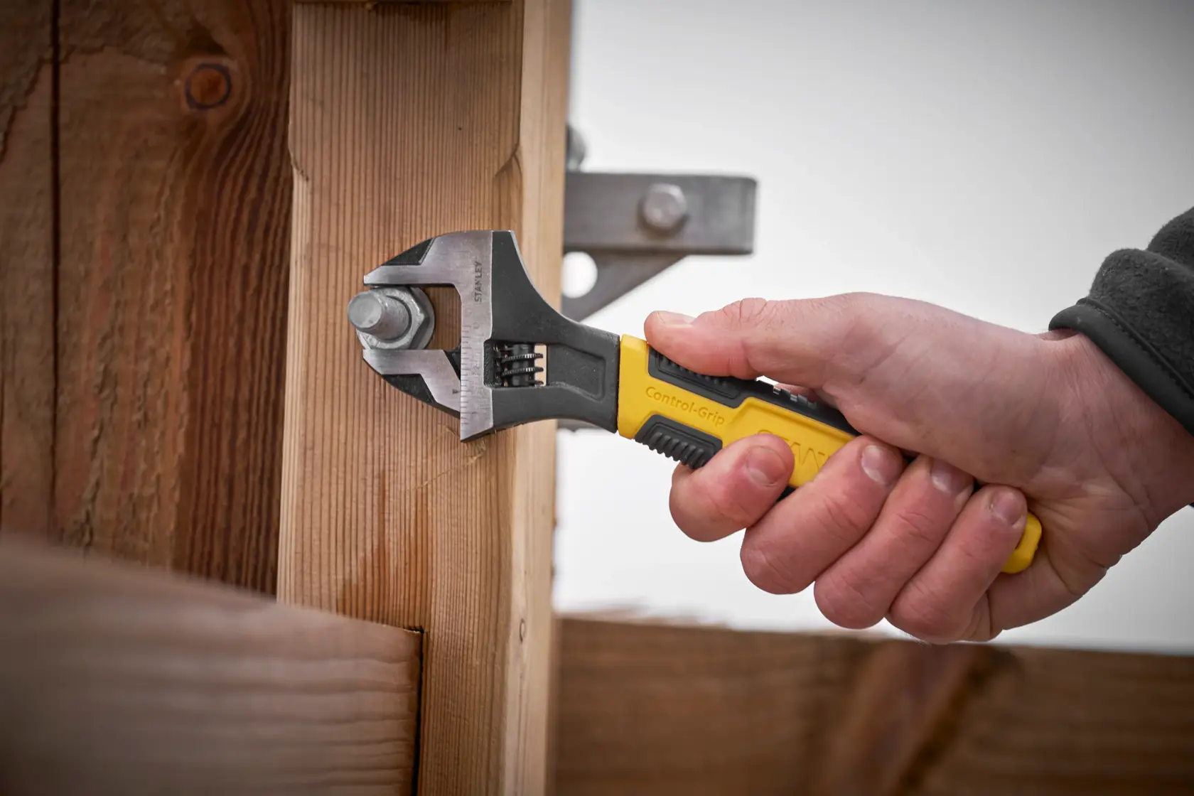 Llave ajustable STANLEY 0-90-948 con mango amarillo y negro utilizada para apretar un perno en estructura de madera.