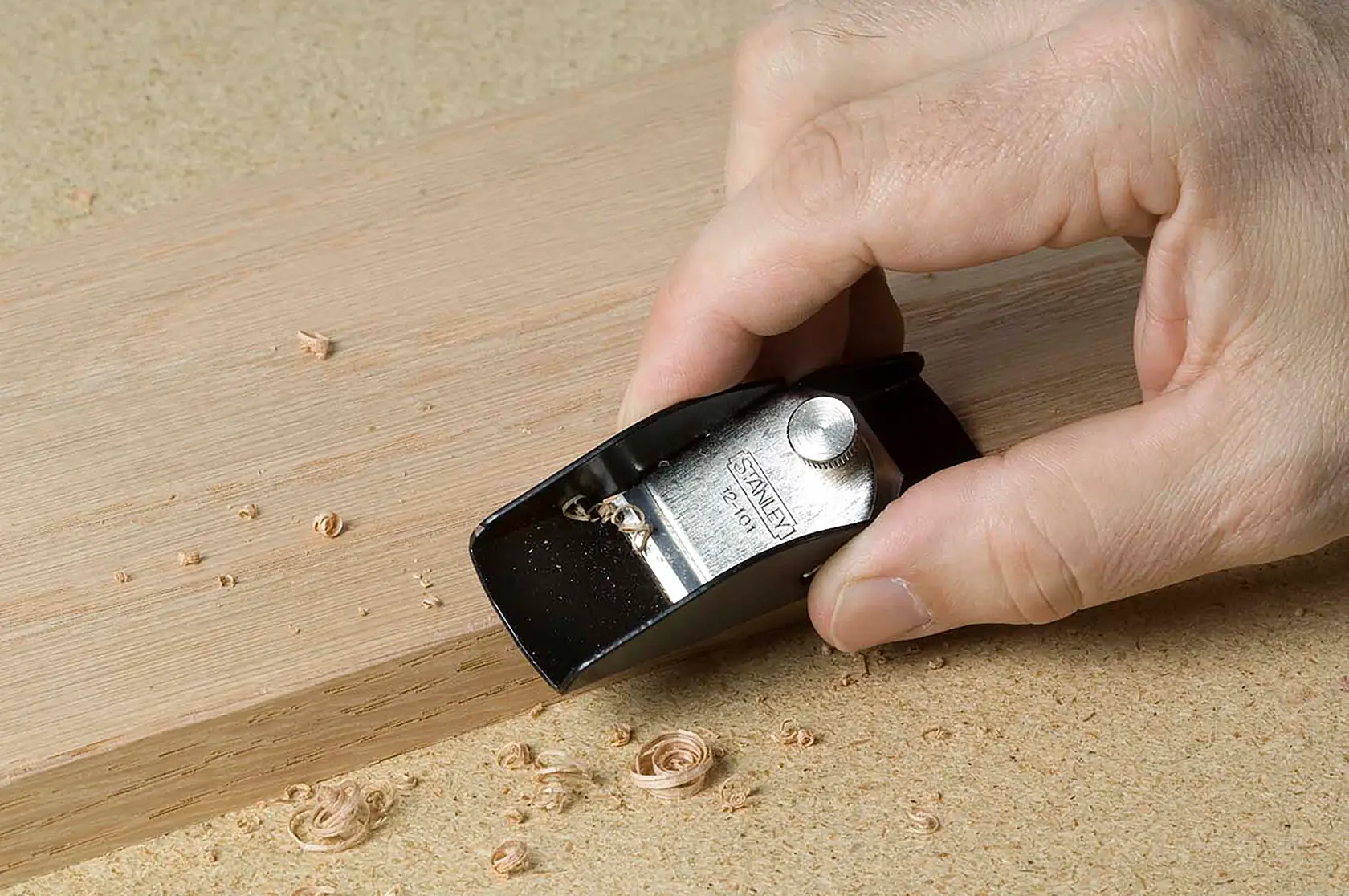 Fotografía de un cepillo de mano STANLEY 12-101 alisando el borde de una tabla de madera.