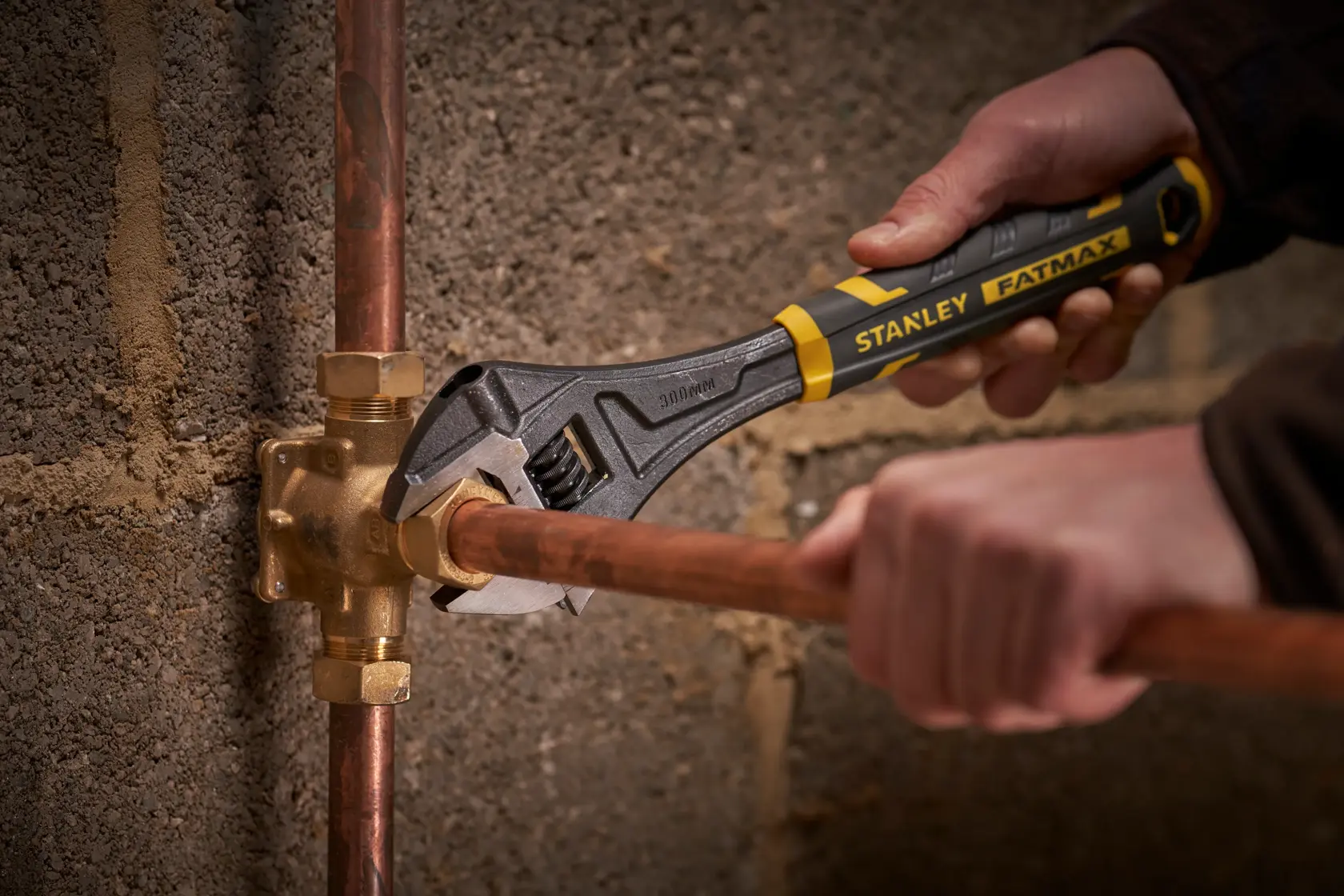 Llave ajustable STANLEY FMHT13128-0 girando unión de tubería sobre pared de hormigón.