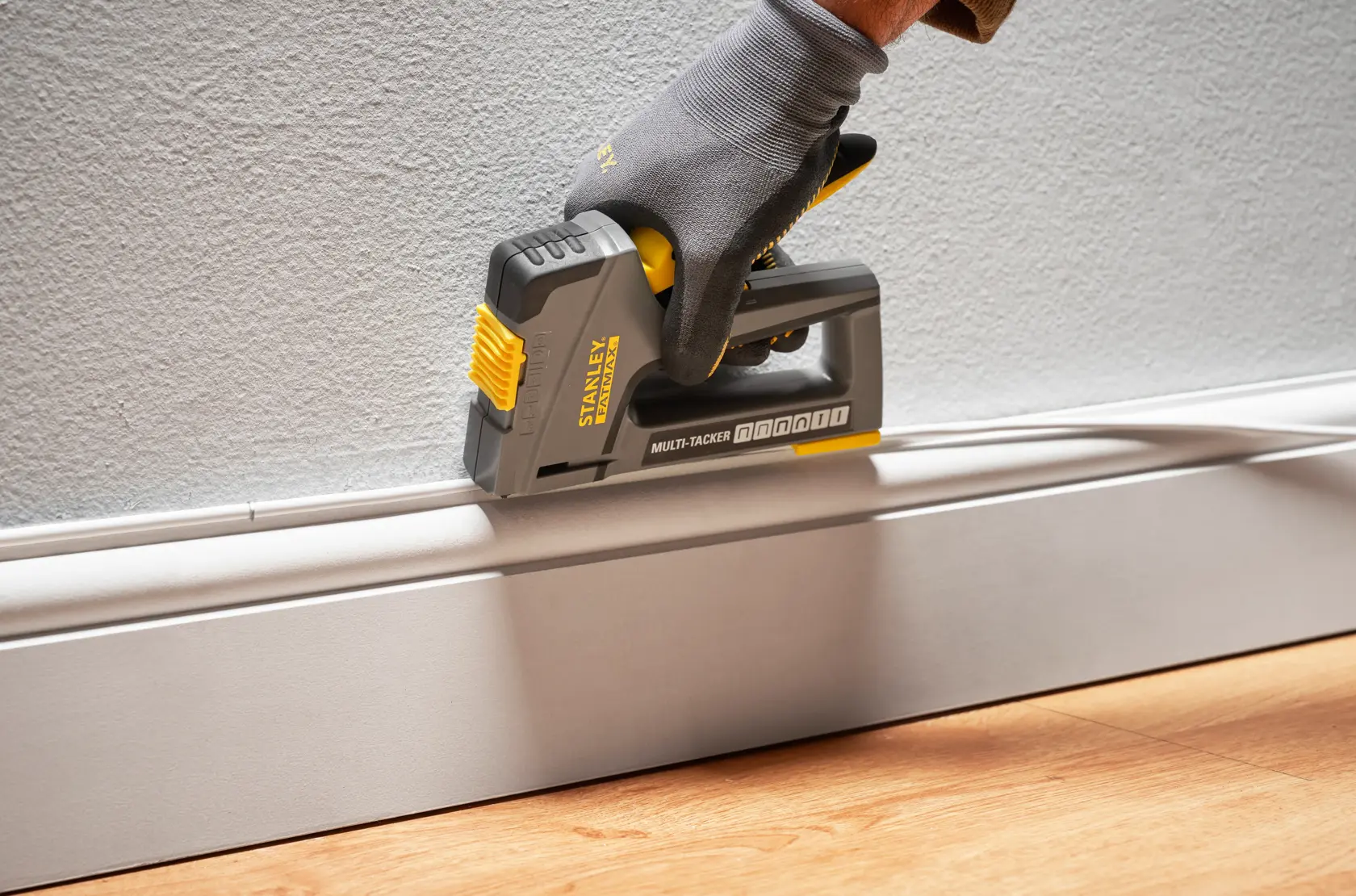 Foto del multi-tacker STANLEY FMHT6-70868 usado para fijar moldura a la pared, sostenido por mano enguantada.