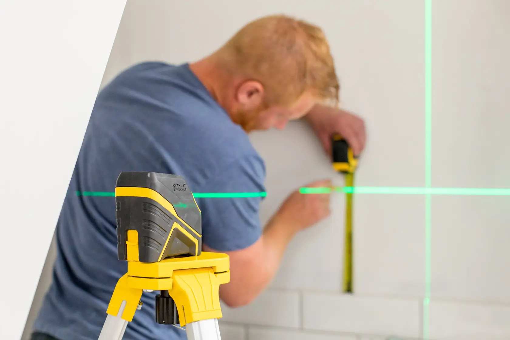 STANLEY FMHT77586-1 nivel láser sobre trípode proyectando líneas verdes, persona mide la pared.