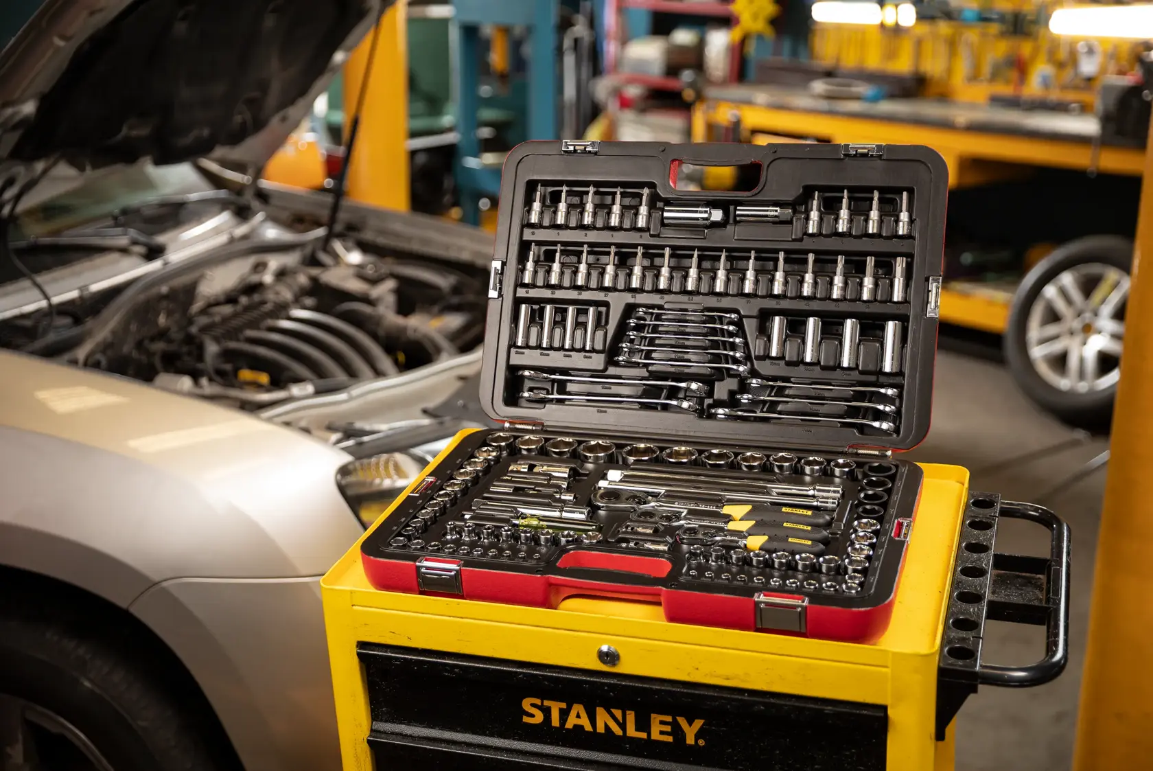 Juego de herramientas mecánicas STANLEY R99-120LA abierto sobre carro de herramientas amarillo, taller automotriz de fondo.