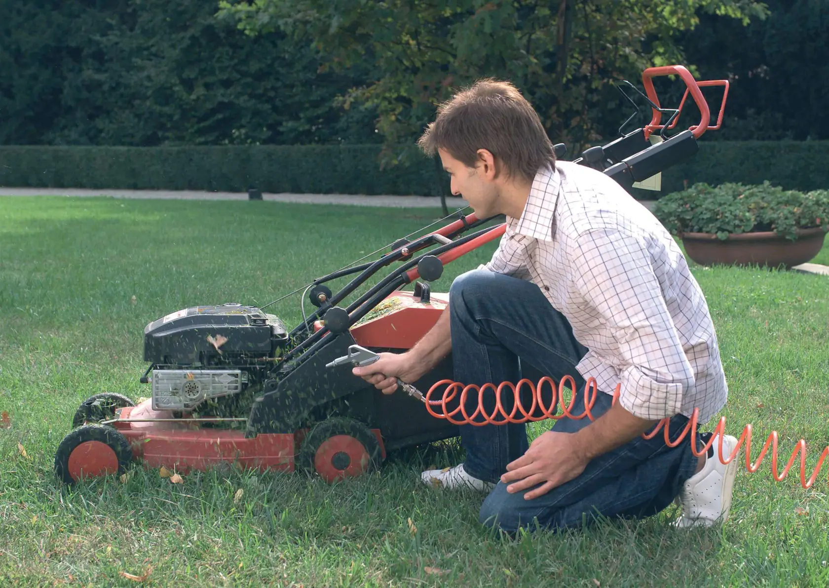 STANLEY SCK6-LA fotografía de compresor de aire limpiando cortacésped rojo con manguera espiral en jardín.