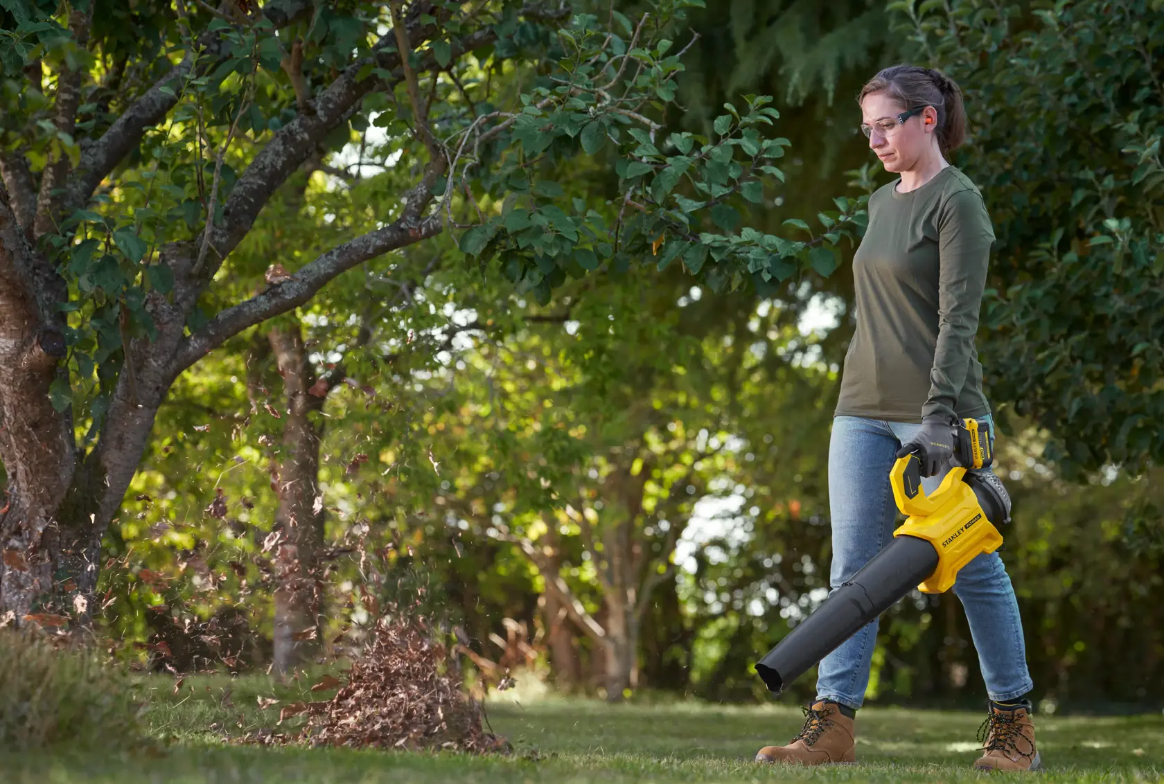 Soplador de hojas STANLEY SFMCBL730B en uso al aire libre, diseño amarillo y negro, soplando hojas bajo un árbol.