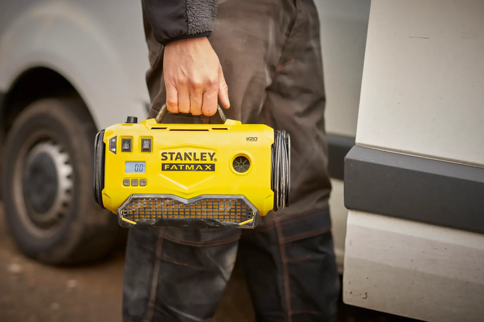 Stanley SFMCE520B inflador portátil amarillo sostenido por el asa, usado al aire libre cerca de un vehículo.