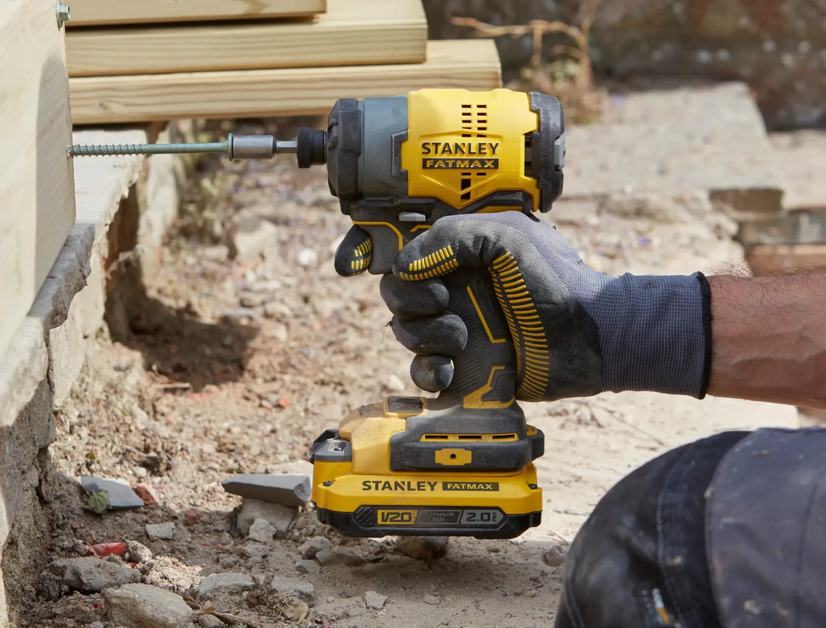 Stanley SFMCF810B taladro de impacto sujetado por una mano enguantada atornillando en madera, entorno exterior.