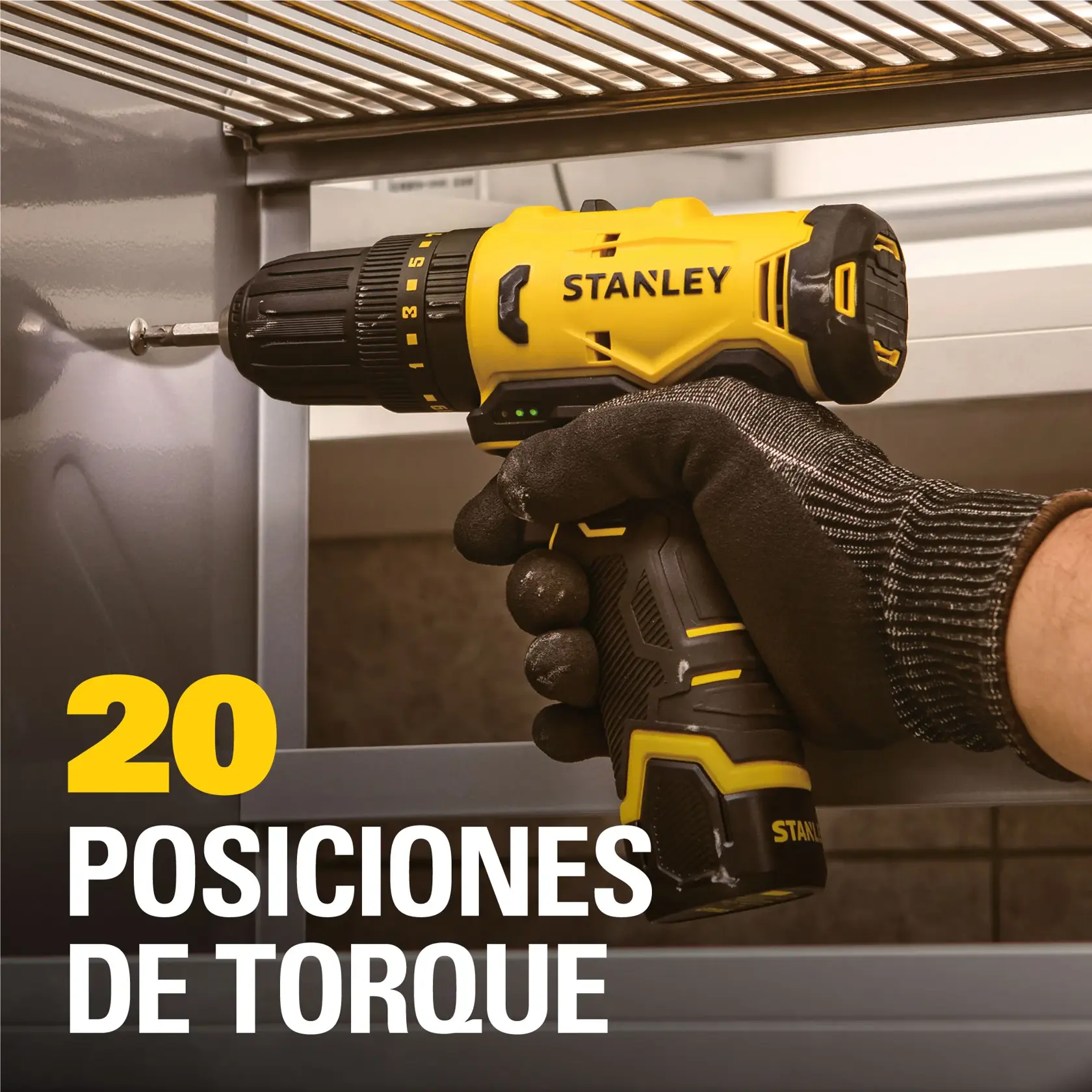 Una persona con un guante de trabajo usa un taladro inalámbrico Stanley amarillo y negro para atornillar un tornillo en una superficie metálica. El texto en la imagen dice '20 posiciones de torque'.