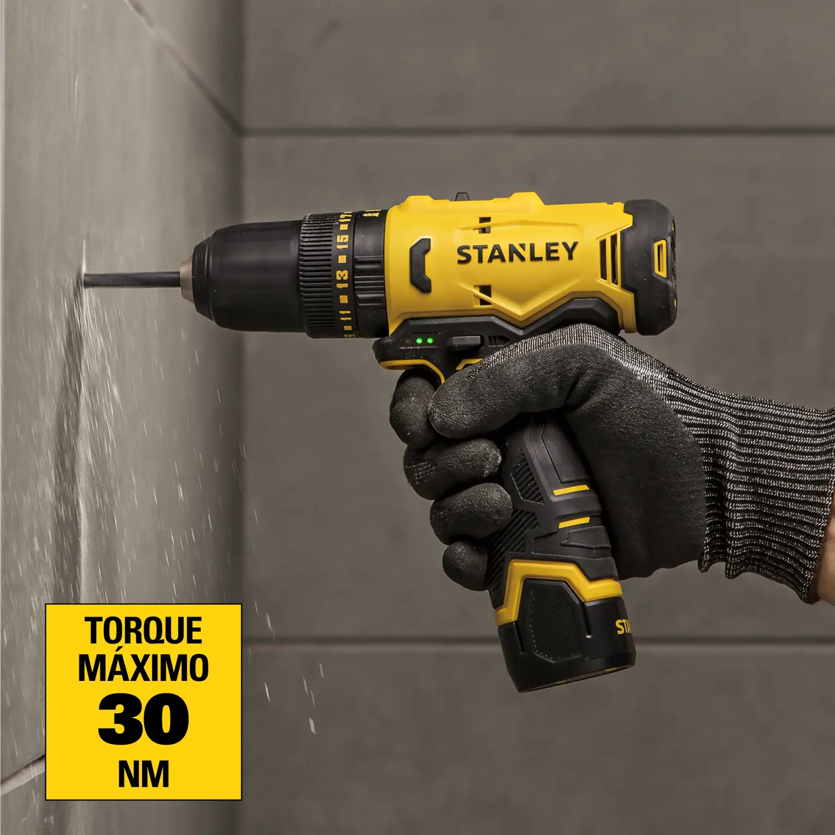 Primer plano de una mano con guante de trabajo negro usando un taladro inalámbrico STANLEY amarillo y negro (SKU: SCH10D2K) para taladrar una pared. Una etiqueta amarilla en la esquina inferior izquierda dice: 'Torque máximo 30 Nm.'