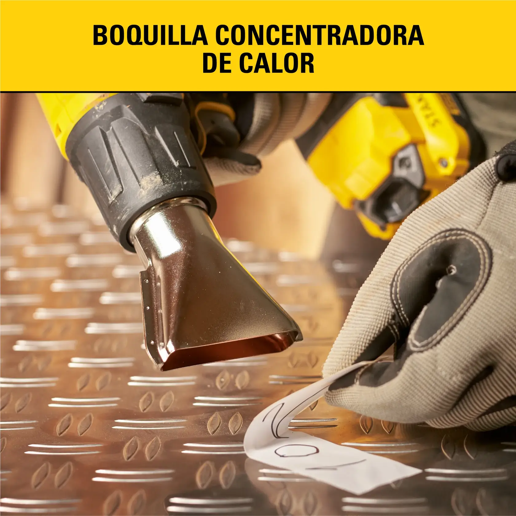 Primer plano de una pistola de calor amarilla y negra con una boquilla concentradora de calor, utilizada sobre una superficie metálica. Una mano con guante sostiene un material cerca de la boquilla. El texto superior dice: 'Boquilla concentradora de calor'.