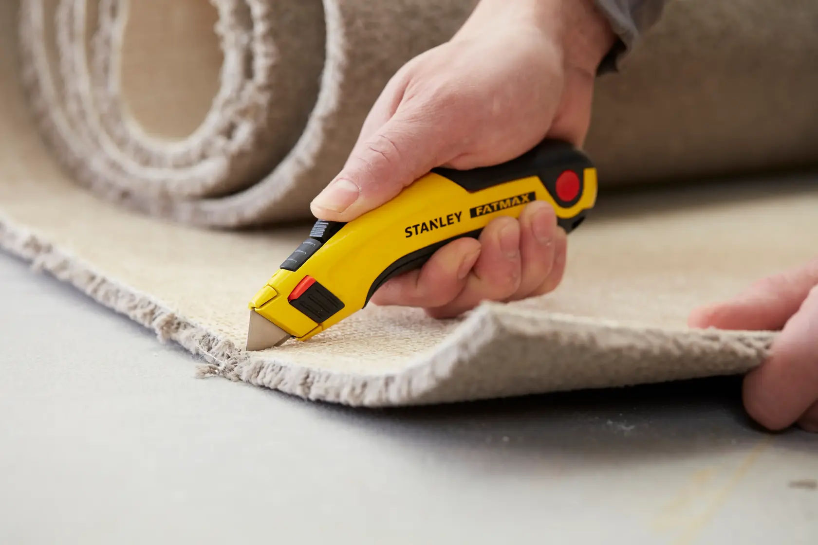 STANLEY 0-11-700 cuchillo de uso general cortando alfombra, foto de cerca, mango amarillo y negro, serie FatMax.