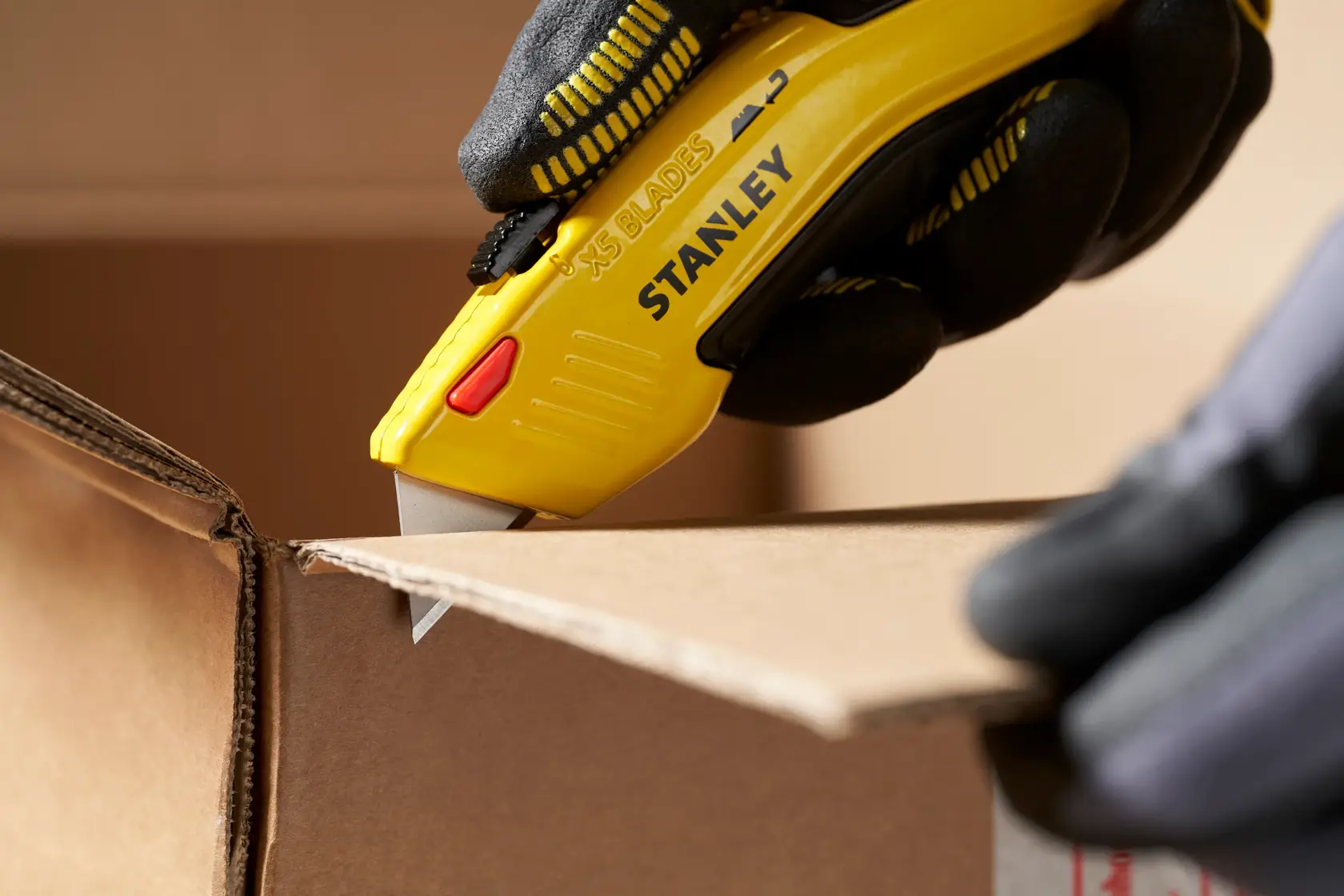 STANLEY 0-11-921 cuchillo multiusos cortando cartón, primer plano, mango amarillo, mano enguantada.