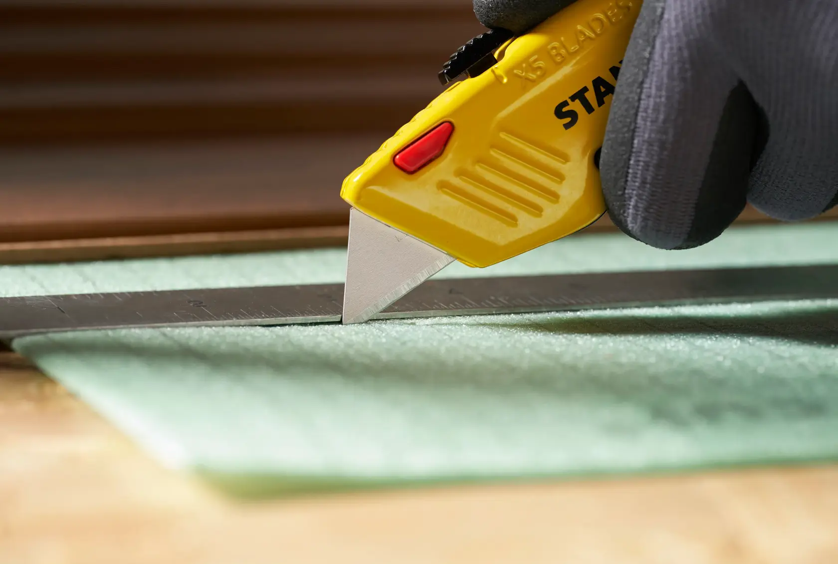 STANLEY 0-11-921 cuchillo utilitario con mango amarillo cortando material junto a una regla metálica, vista de cerca.
