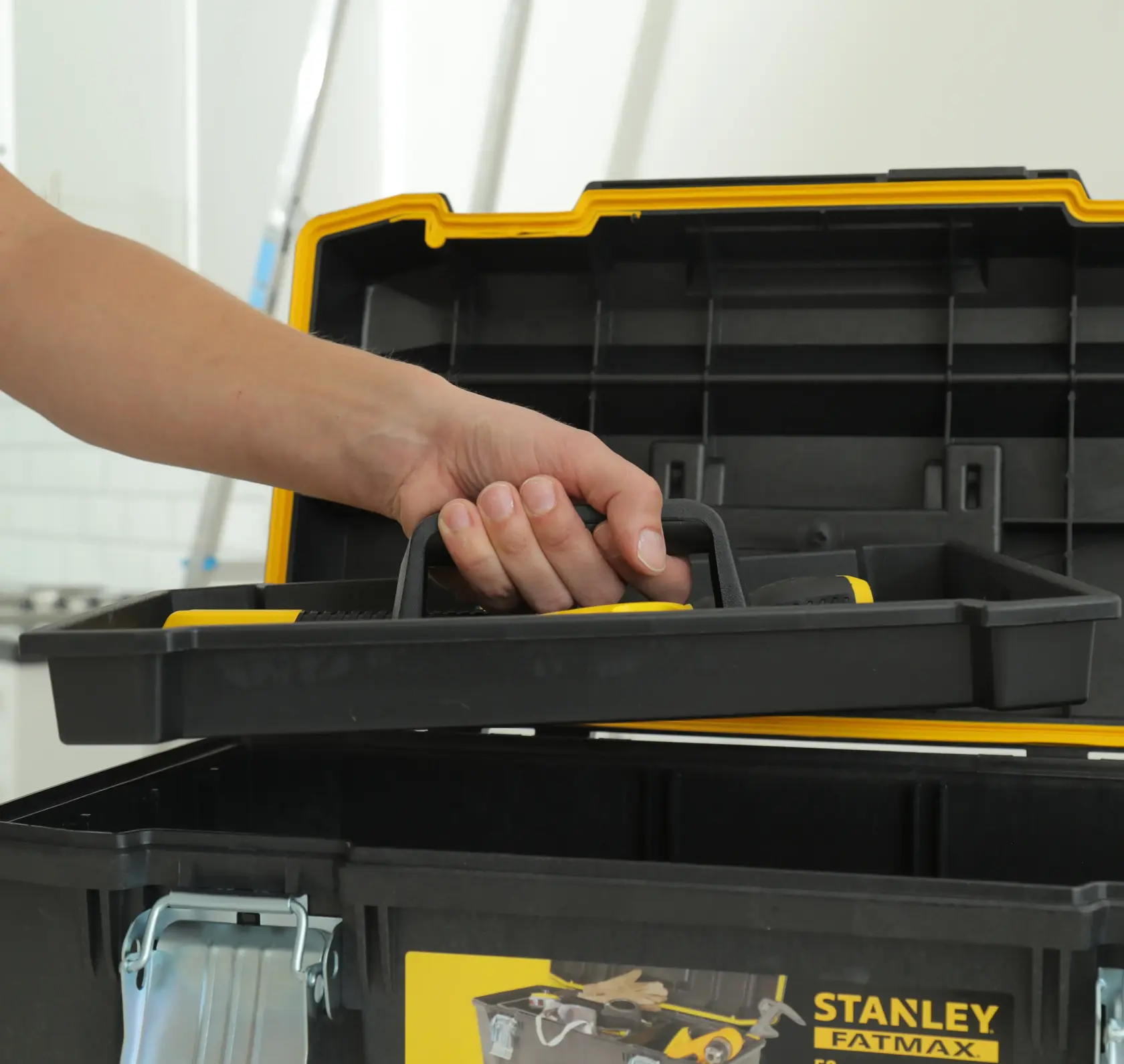 STANLEY 023001W caja de herramientas en primer plano con una mano levantando la bandeja extraíble, plástico negro y amarillo.