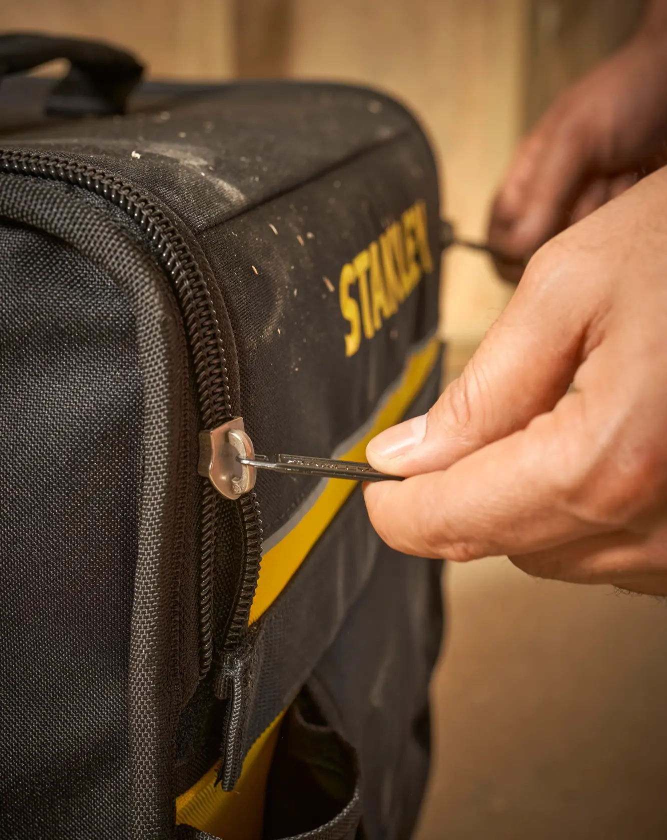 STANLEY 1-97-515 bolsa de herramientas fotografía, primer plano de mano usando cremallera en bolsa negra y amarilla.
