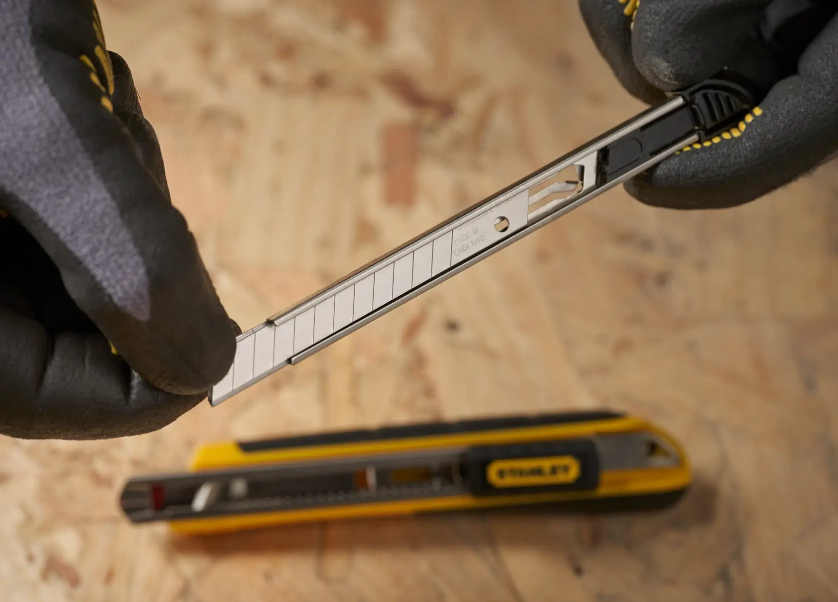 Cuchilla para cuchillo Stanley 11-300 sostenida con guantes, vista cercana con otro cuchillo Stanley amarillo debajo.