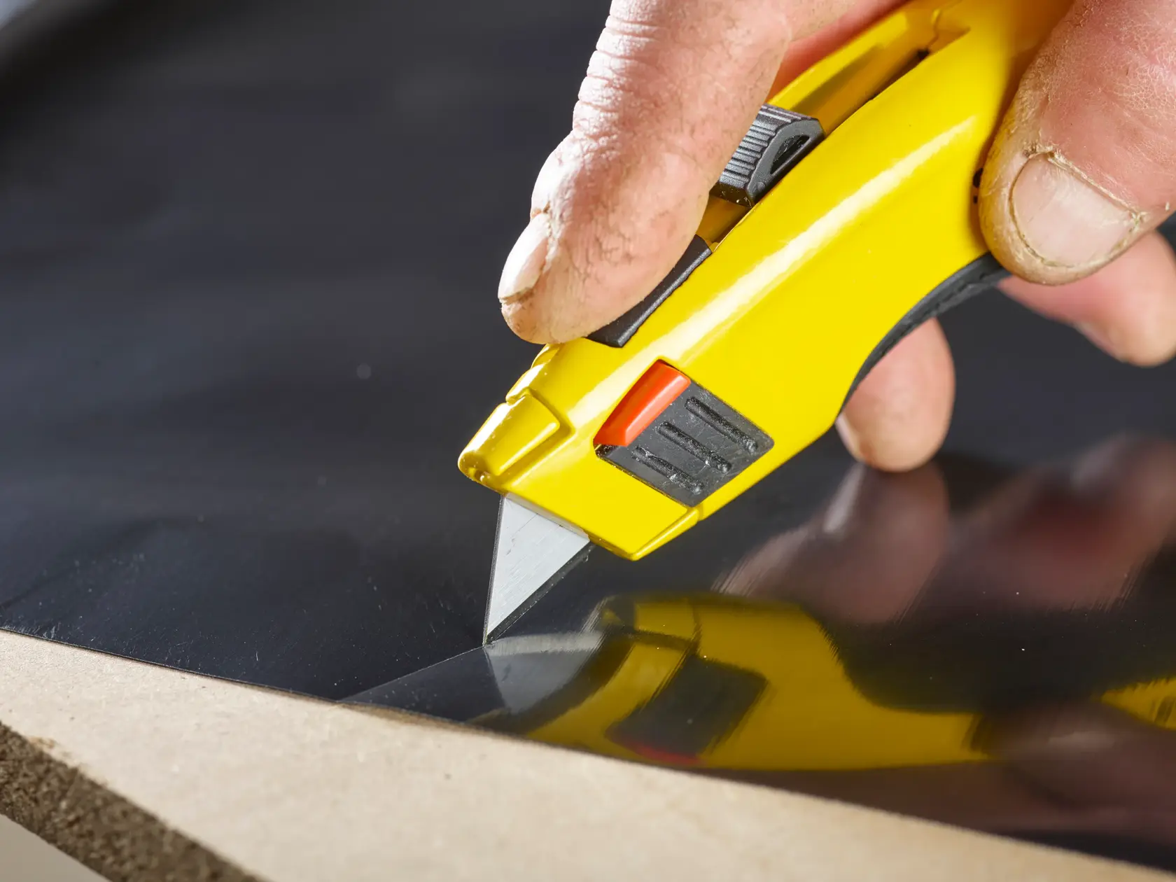 STANLEY 2-11-921 cuchillo multiusos con mango amarillo cortando lámina negra, primer plano, producto en uso.