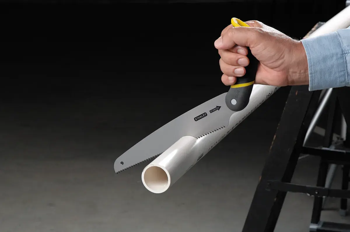 STANLEY 20-092 sierra manual cortando tubo de PVC blanco, vista lateral cercana con mango negro y amarillo.