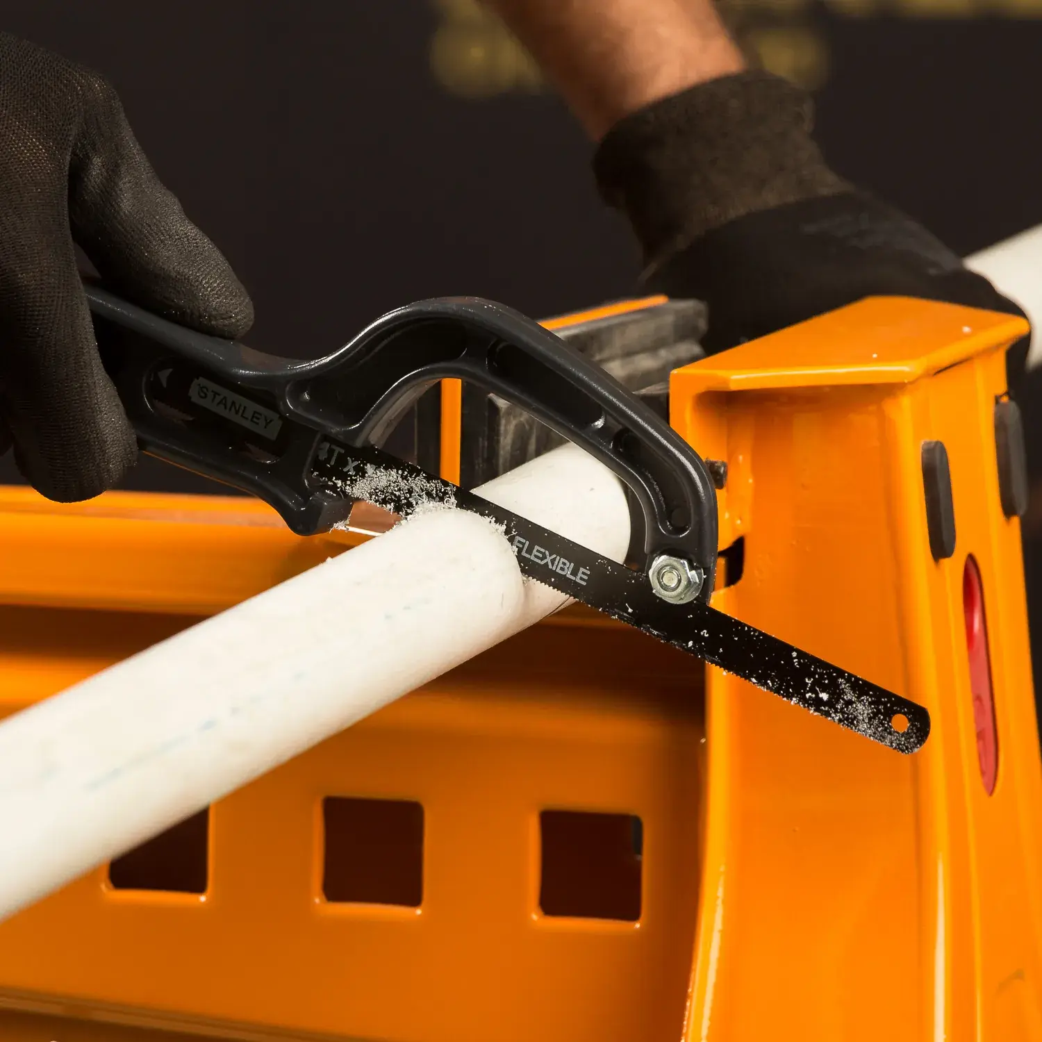 STANLEY 20-807 mini segueta cortando tubo de PVC blanco sobre banco de trabajo naranja, ángulo lateral cercano.