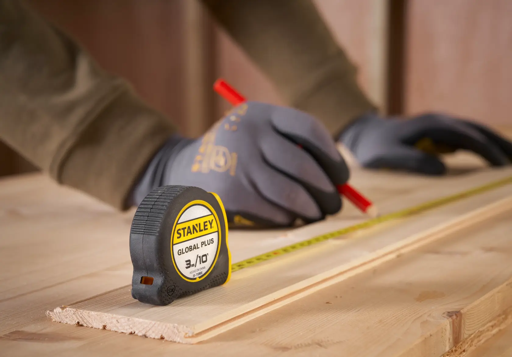 Fotografía de cinta métrica STANLEY 30-710MX sobre madera, guantes sosteniendo lápiz y cinta para carpintería.