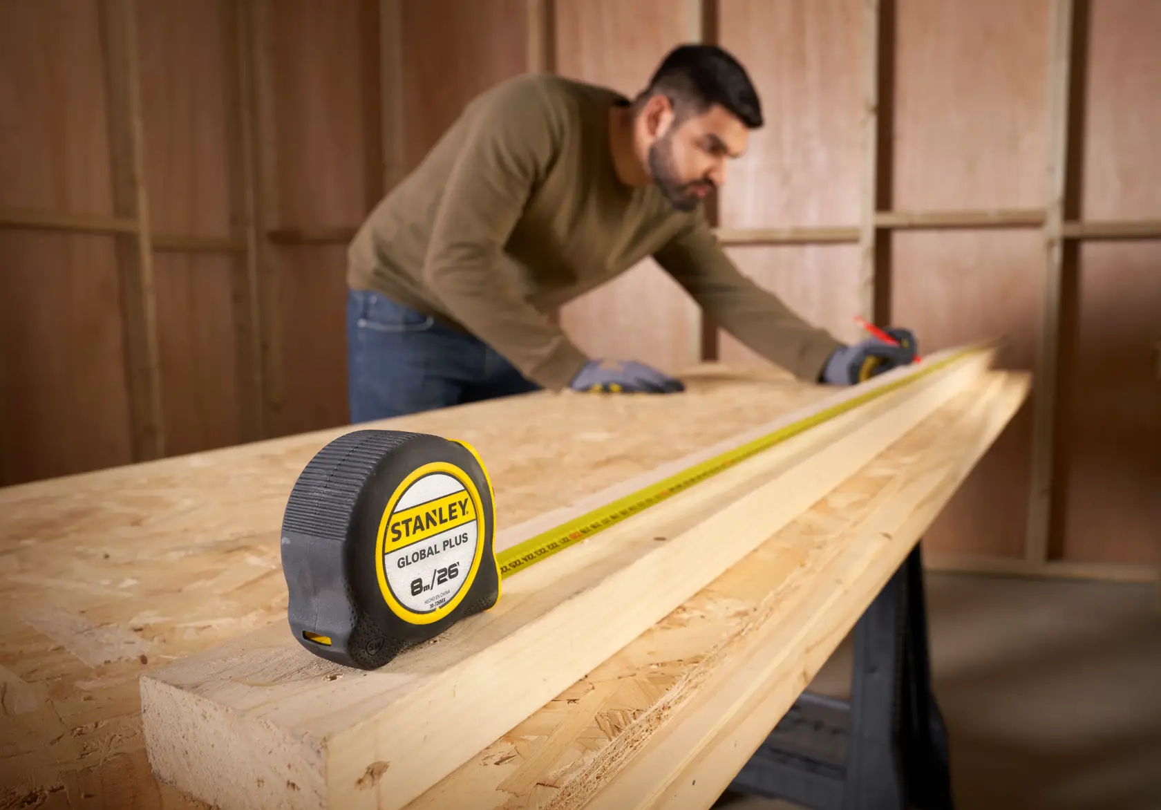 Cinta métrica STANLEY 30-726MX sobre una tabla de madera con persona midiendo madera en taller.