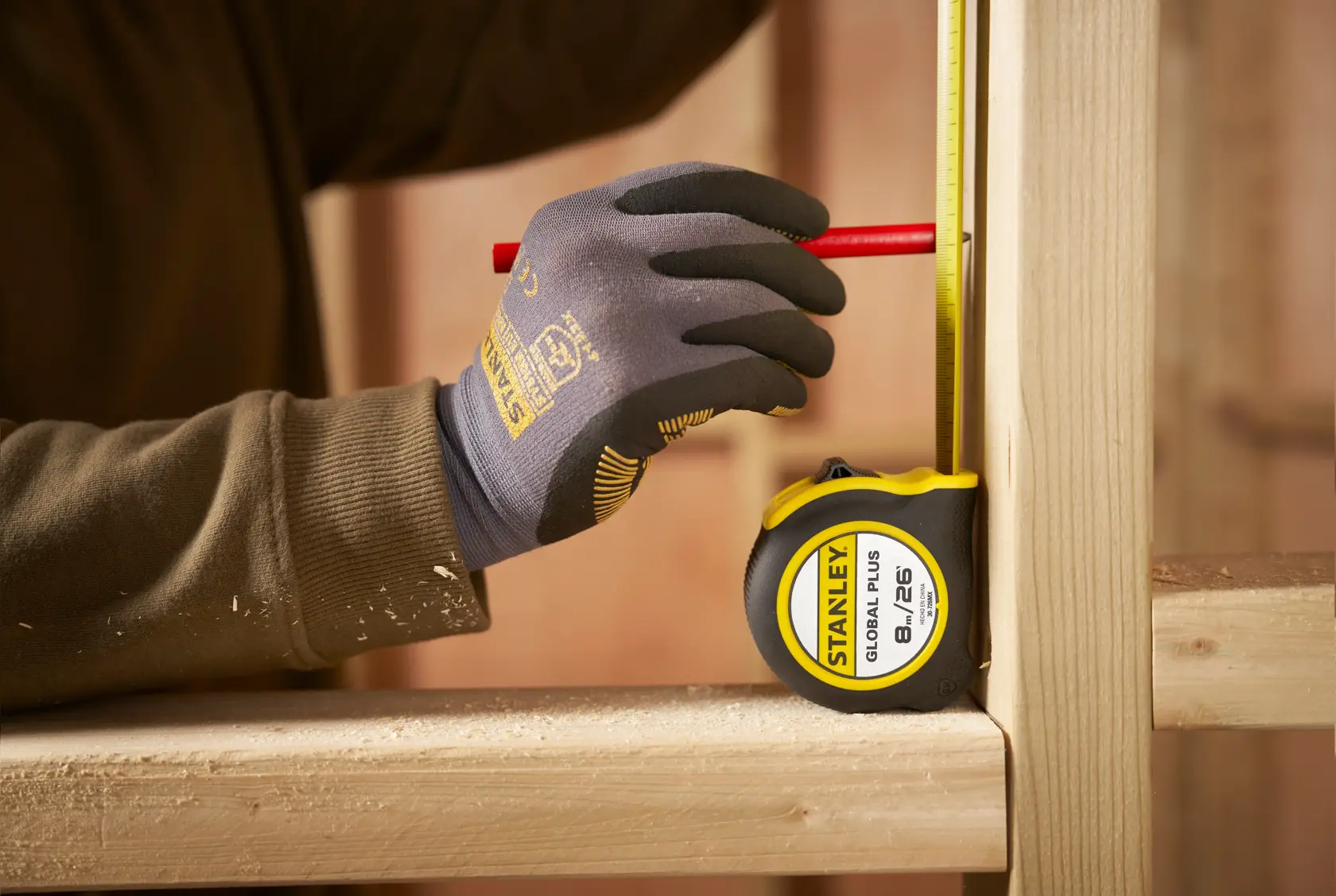 Fotografía de la cinta métrica STANLEY 30-726MX en uso, midiendo marco de madera, operario con guantes y marcando con lápiz.