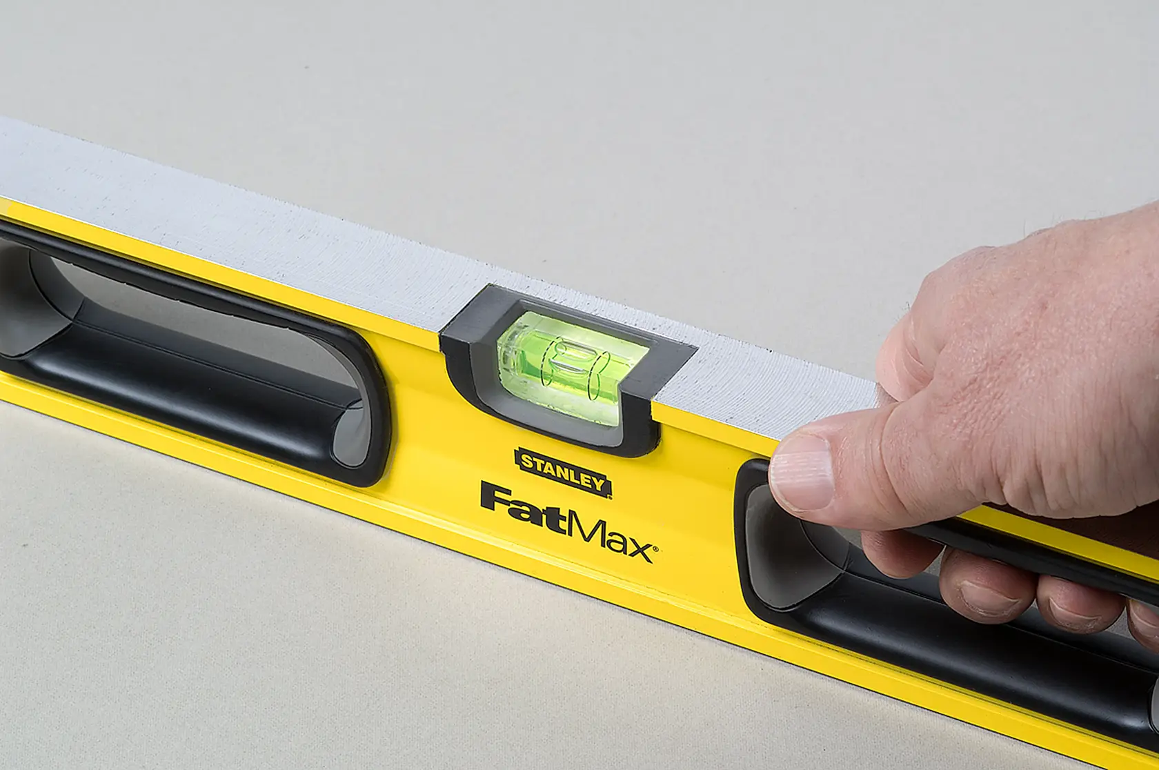 Foto del nivel STANLEY 43-524 FatMax sostenido en mano, cuerpo amarillo, asas negras y vial visible.