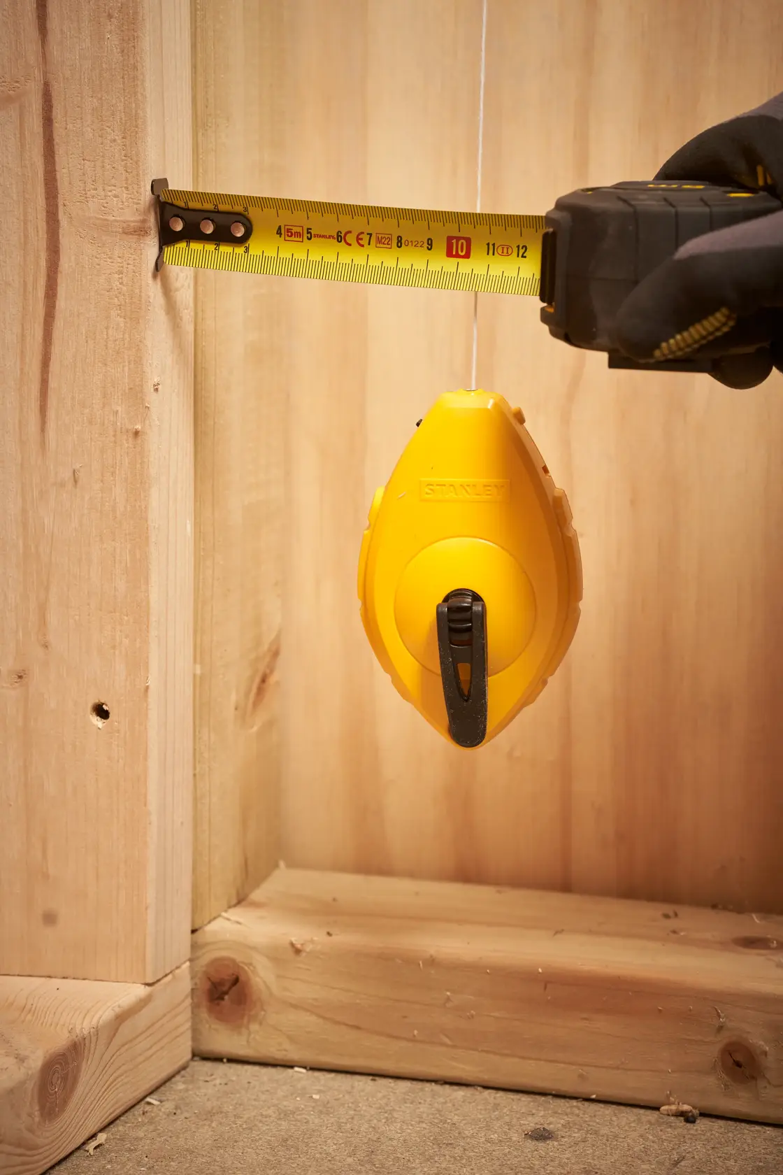 STANLEY 47-440 carrete de línea de tiza con cinta métrica en uso, herramienta amarilla sobre madera, primer plano.