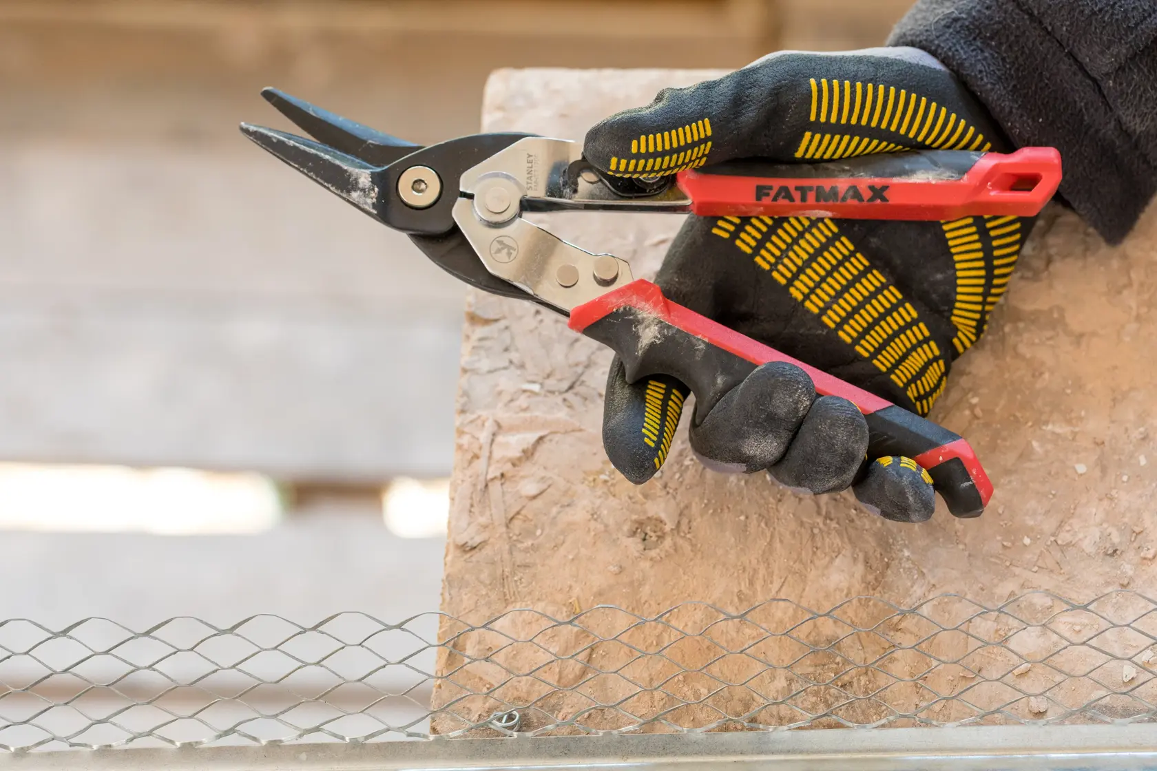 Stanley FMHT73755 tijeras para metal con mango rojo en mano enguantada, ángulo lateral, corta malla metálica.