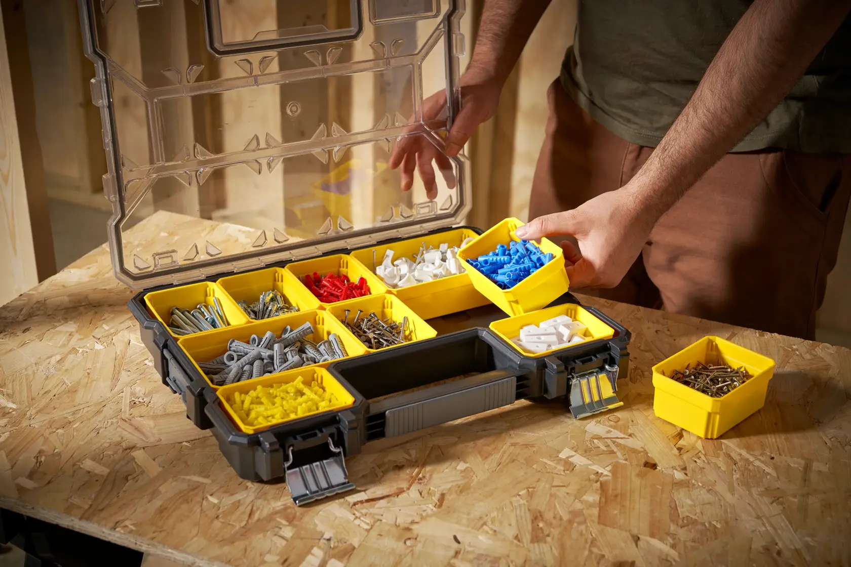 Organizador STANLEY FMST14820 con compartimientos amarillos extraíbles llenos de piezas, sobre un banco, vista en ángulo.