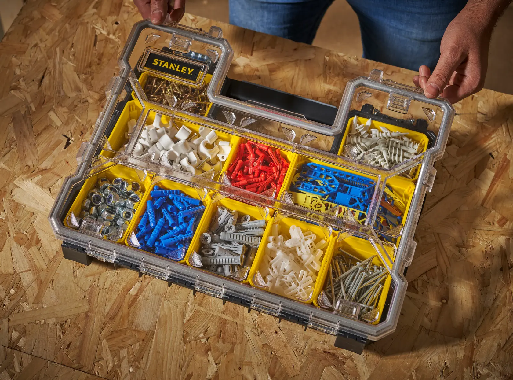Organizador STANLEY FMST14820 con tapa transparente, contiene tacos y herrajes variados en compartimentos amarillos, vista superior angular.