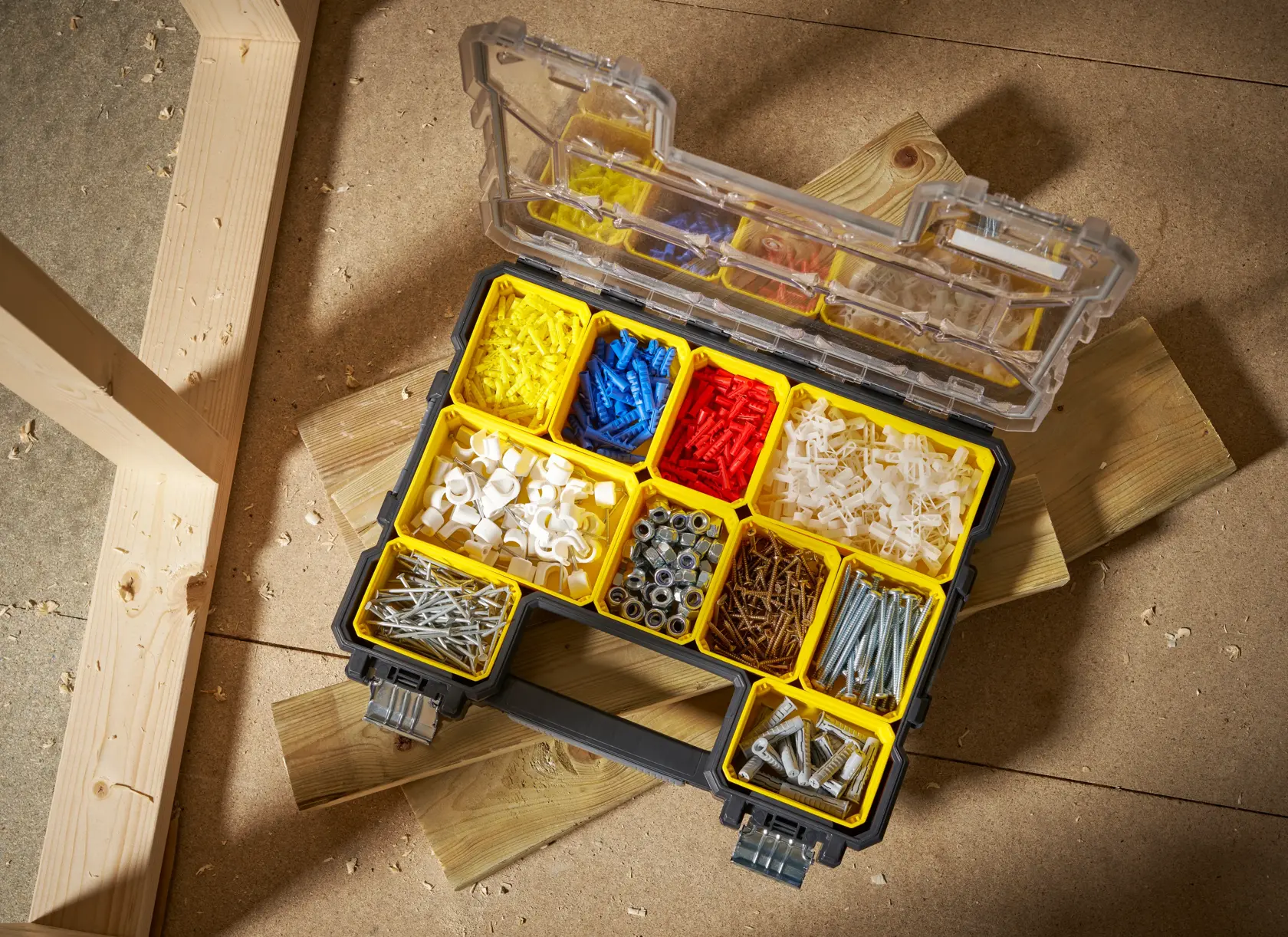 Caja organizadora STANLEY FMST14820 con compartimentos amarillos llenos de piezas variadas, abierta en un taller.
