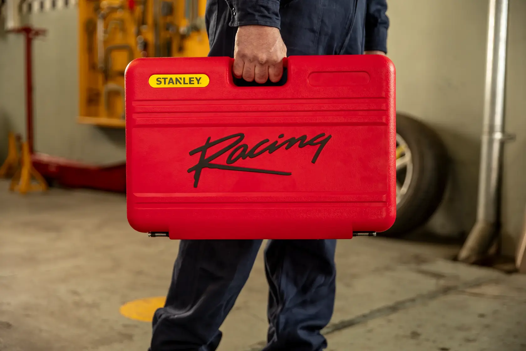 Estuche de herramientas rojo STANLEY R99-120LA con logo Racing negro, sostenido por persona en taller.