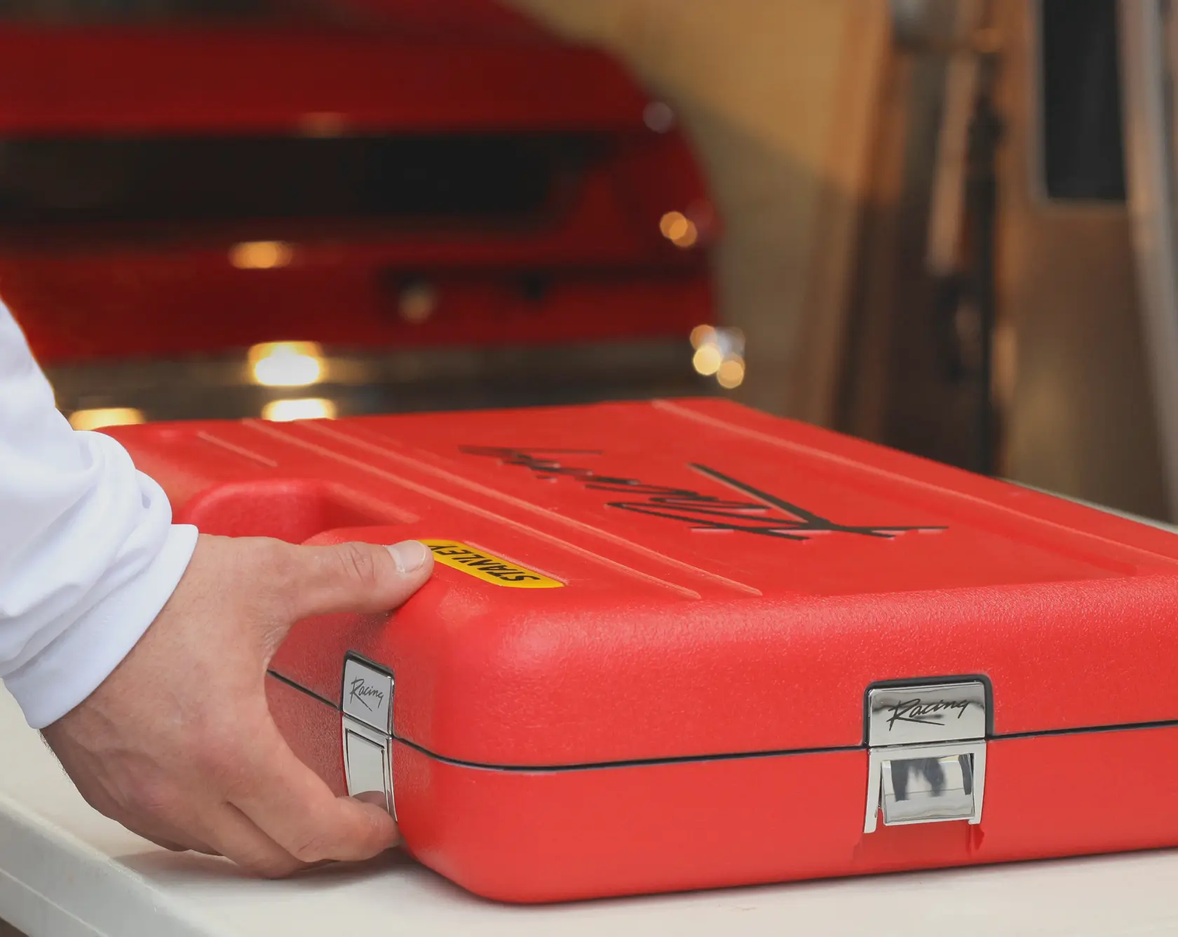 Maletín rojo de plástico rígido STANLEY R99-150LA con cierres metálicos, sobre una mesa con una mano sujetando el lateral.