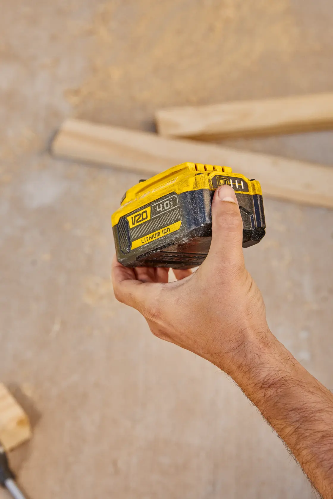 Fotografía de batería de ion de litio STANLEY SB204-KR V20 sostenida en mano, fondo de madera de construcción.