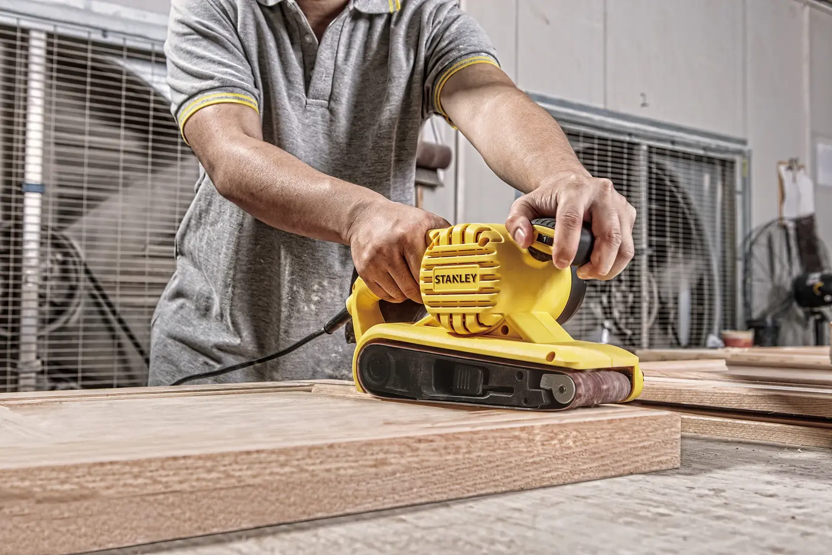 Lijadora de banda Stanley SB90-B2C en uso sobre madera, herramienta amarilla manual, taller.