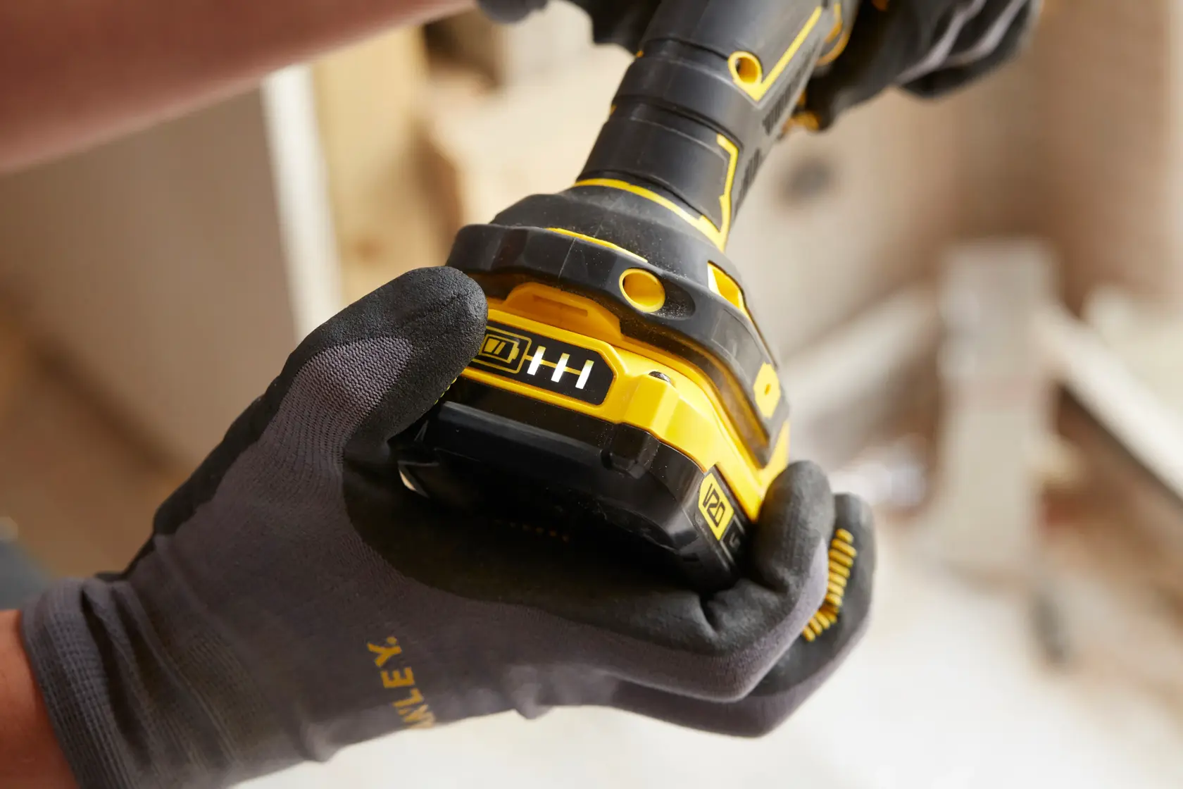 Stanley SBD710C2K-BR taladro inalámbrico sostenido por manos enguantadas, batería y mango en primer plano.