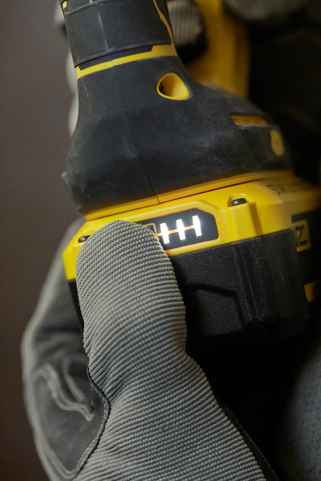 STANLEY SBH900 taladro en primer plano con mano enguantada pulsando indicador de batería, amarillo y negro, fotografía