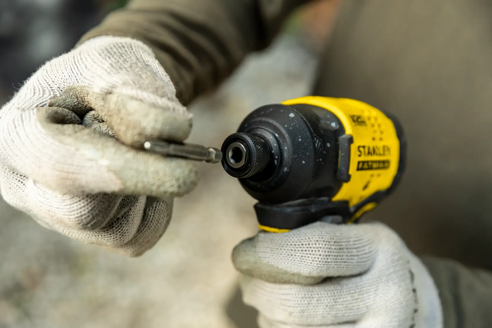 Destornillador de impacto Stanley SBI811 en primer plano, manos enguantadas insertando una broca, herramienta amarilla y negra.