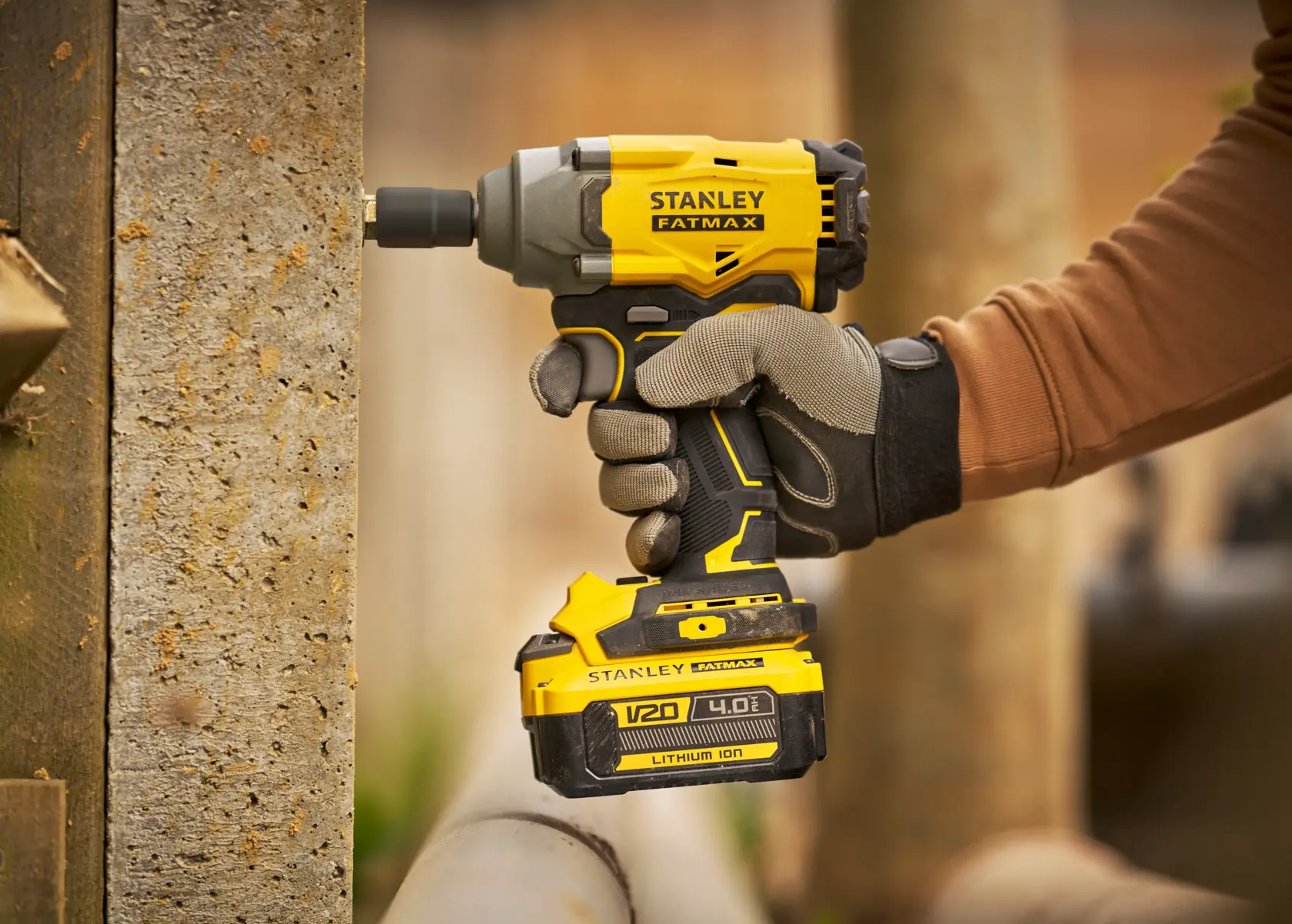 Stanley SBW920 destornillador de impacto inalámbrico en mano enguantada, amarillo y negro, entorno exterior.