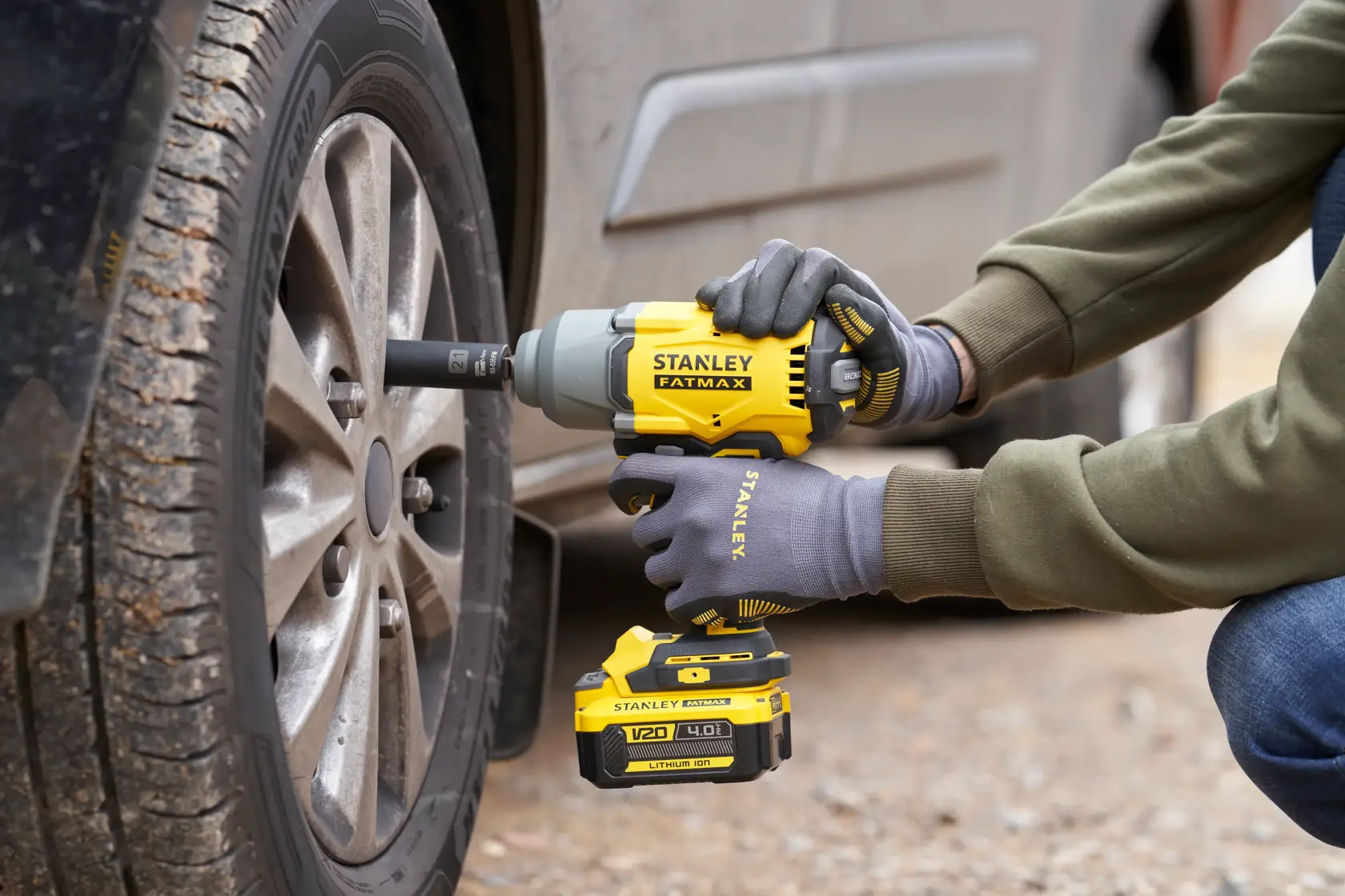 Llave de impacto inalámbrica STANLEY SBW940 en uso, ajustando tuercas de una rueda de coche afuera.
